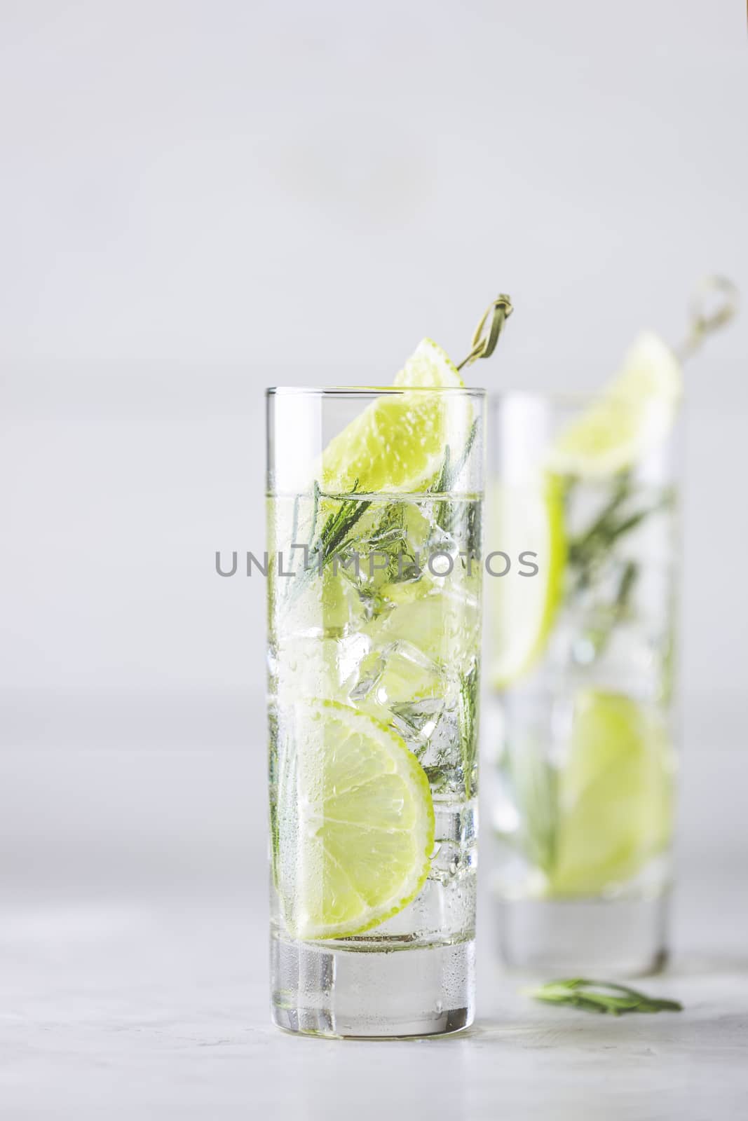 Refreshing lemon lime drink with ice cubes in glass goblets against a light gray background. Summer fresh lemon soda cocktail with rosemary, selective focus.