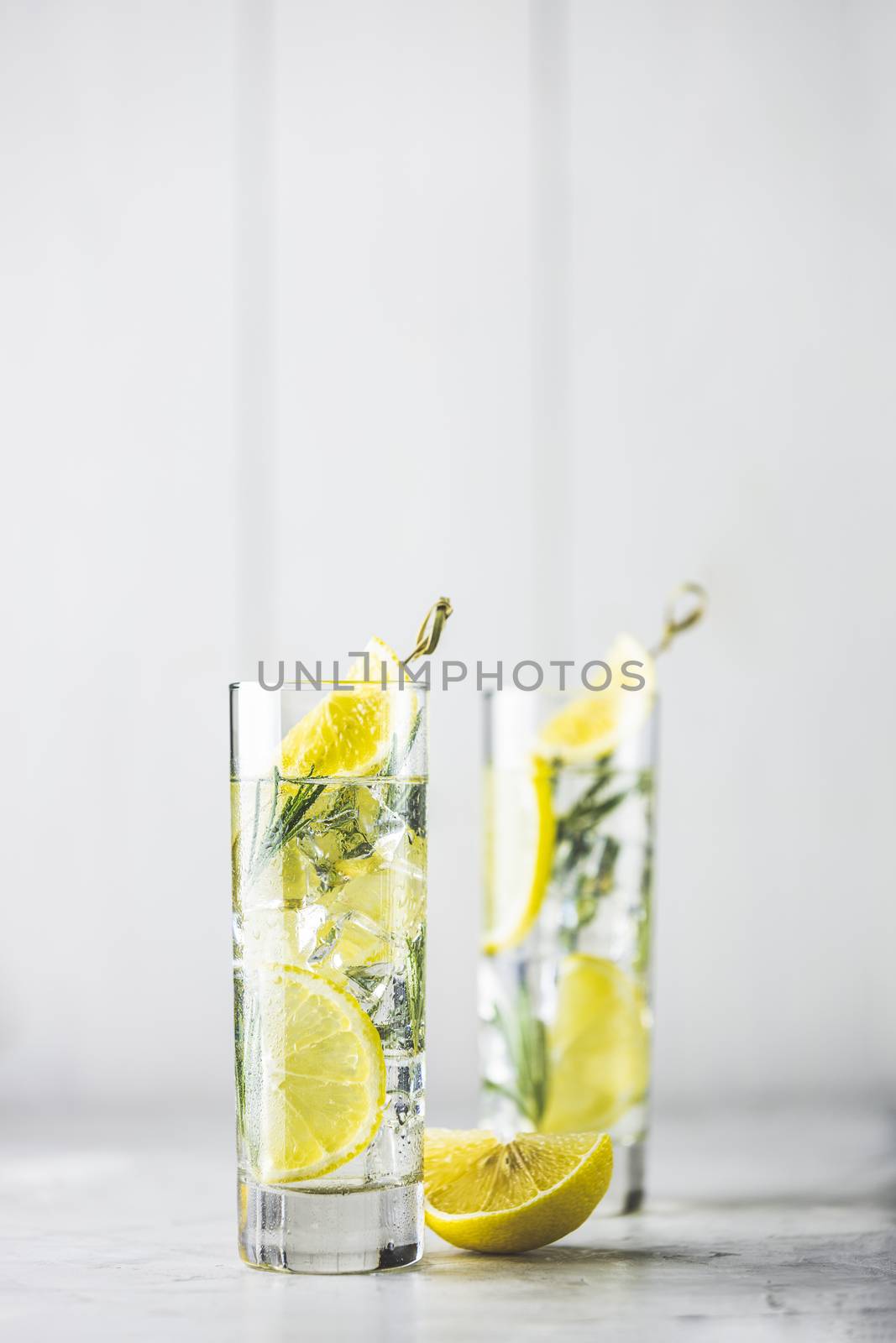 Refreshing lemon lime drink with ice cubes in glass goblets against a light gray background. Summer fresh lemon soda cocktail with rosemary, selective focus