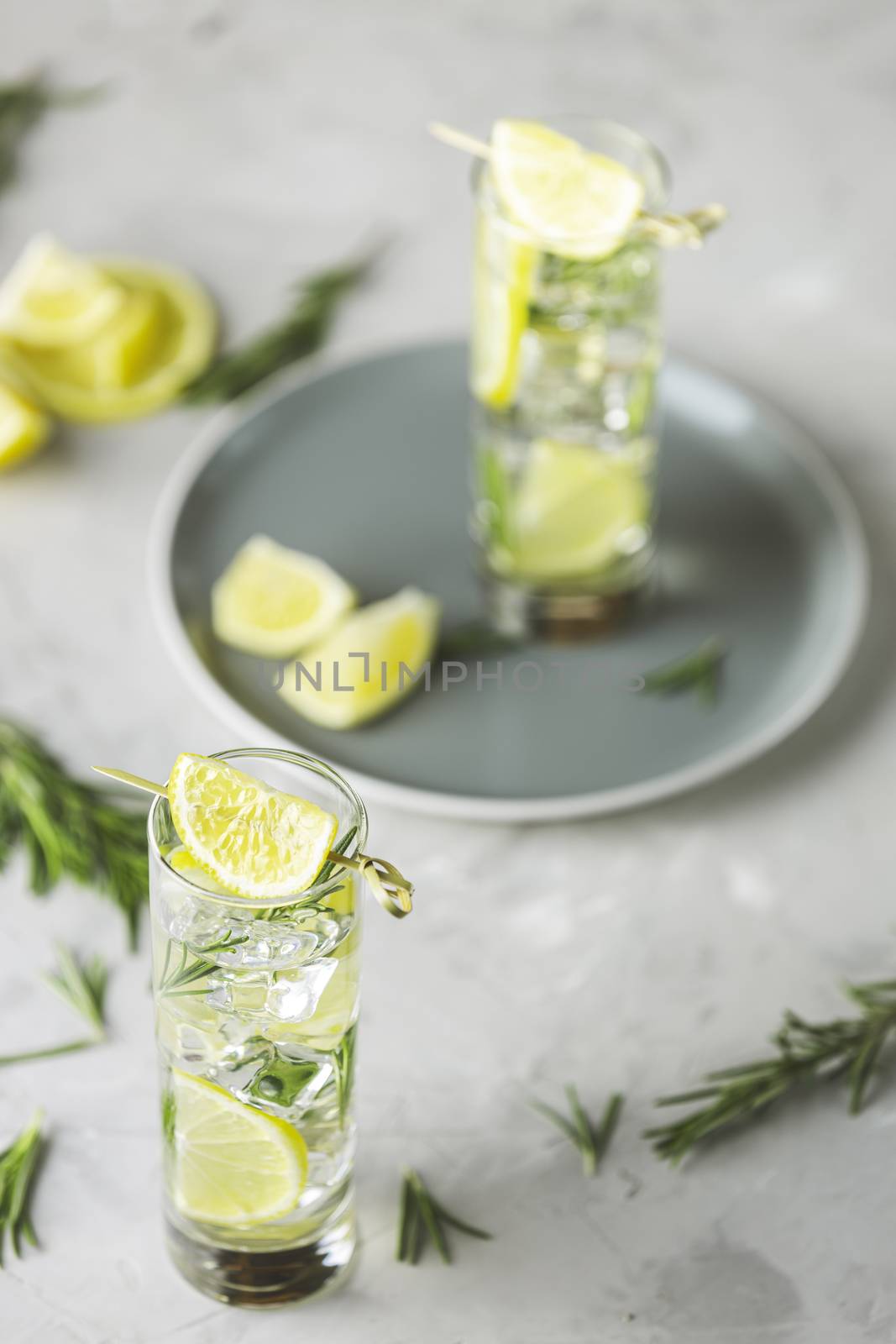 Refreshing lemon lime drink with ice cubes in glass goblets against a light gray background. Summer fresh lemon soda cocktail with rosemary, selective focus.