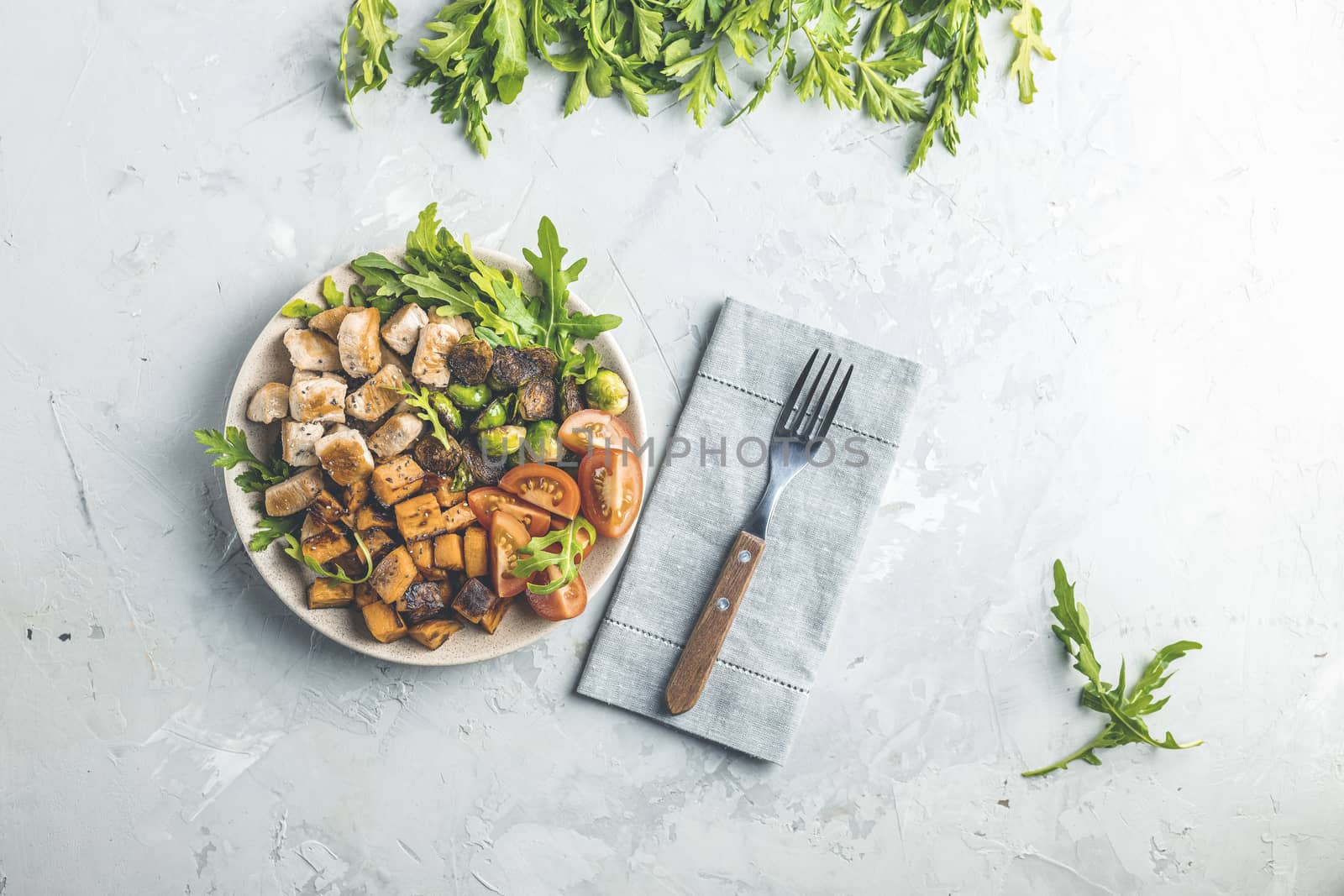 Healthy food. Plate of baking chicken meat, fried sweet potato and brussels sprouts. Top view, light gray concrete surface, flat lay.