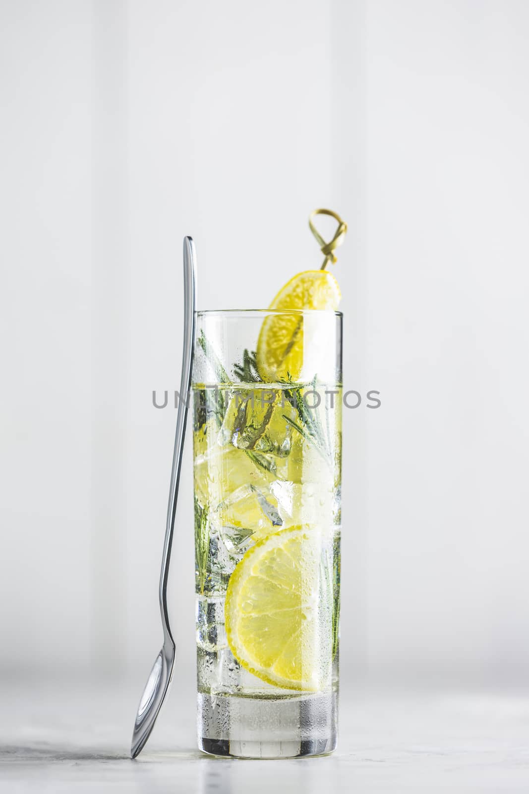 Glass of refreshing lemon lime drink with ice cubes in glass goblets against a light gray background. Summer fresh lemon soda cocktail with rosemary, selective focus