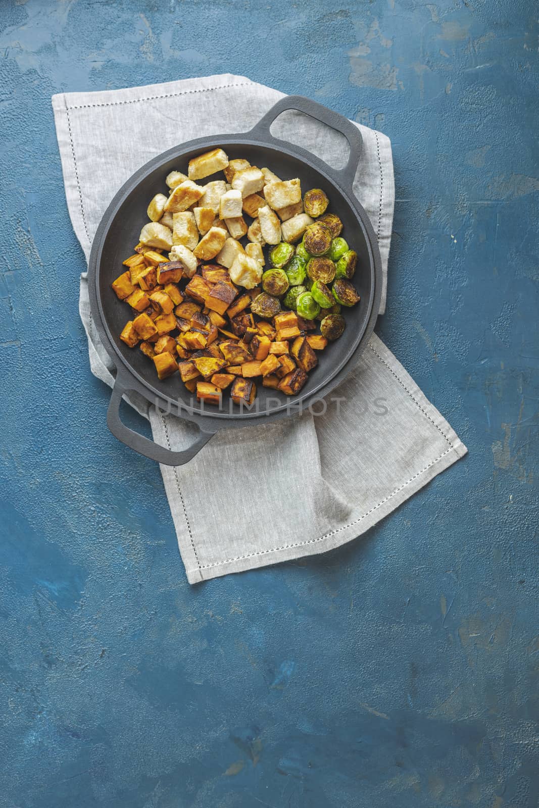 Healthy food. Pan of baking chicken meat, fried sweet potato and brussels sprouts. Top view, classic blue concrete surface, flat lay.