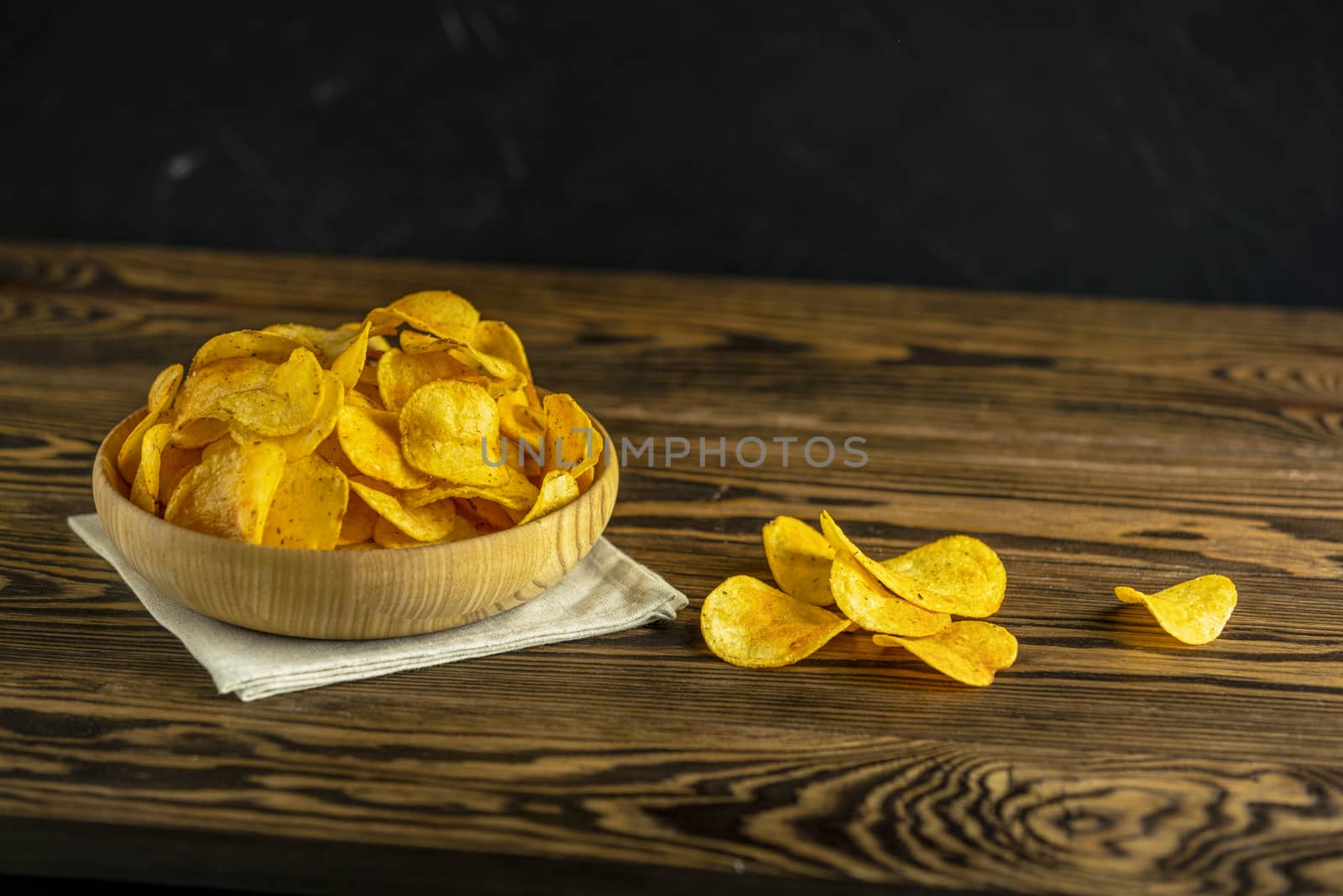 Potato chips in bowl on a wooden background. Salty crisps scattered on a table.