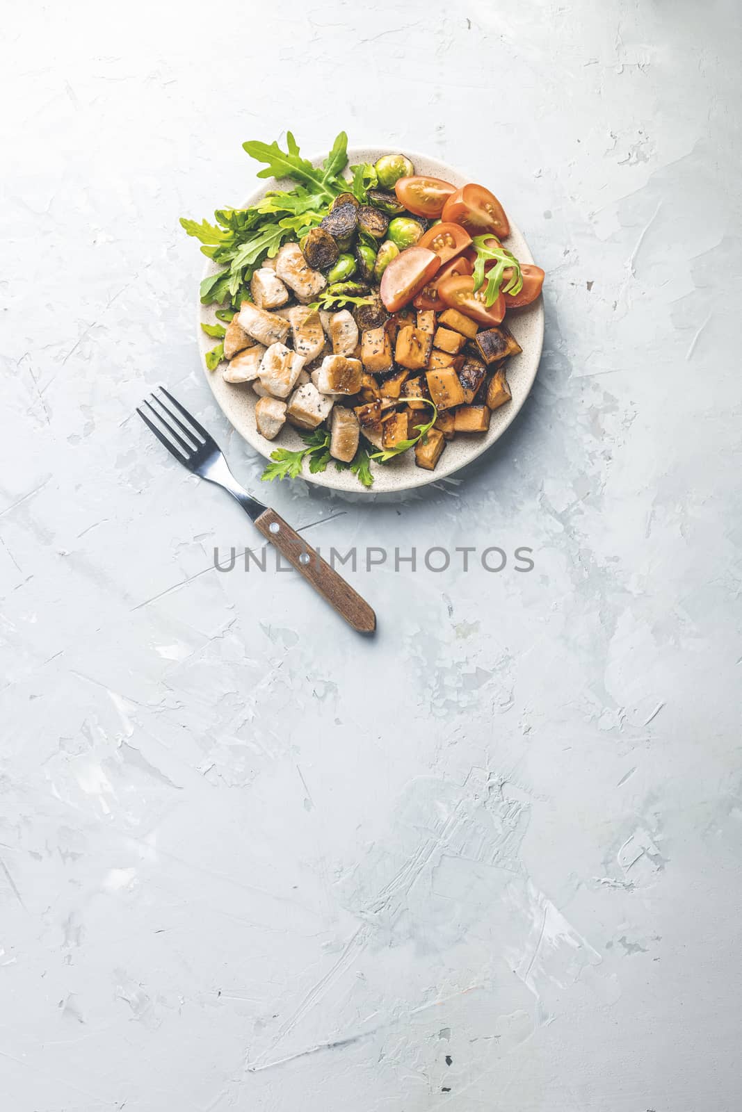 Healthy food. Plate of baking chicken meat, fried sweet potato and brussels sprouts. Top view, light gray concrete surface, flat lay.