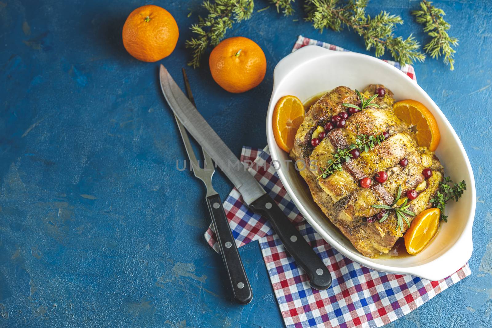 Color of 2020 year. Classic Blue, food trendy background. Roasted pork in white dish, christmas baked ham with cranberries, tangerines, thyme, rosemary, garlic on dark table surface