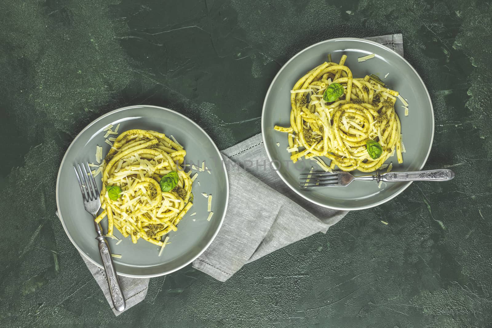 Spaghetti pasta bucatini with pesto sauce and parmesan. Italian traditional perciatelli pasta by genovese pesto sauce in two gray dishes, top view, flat lay