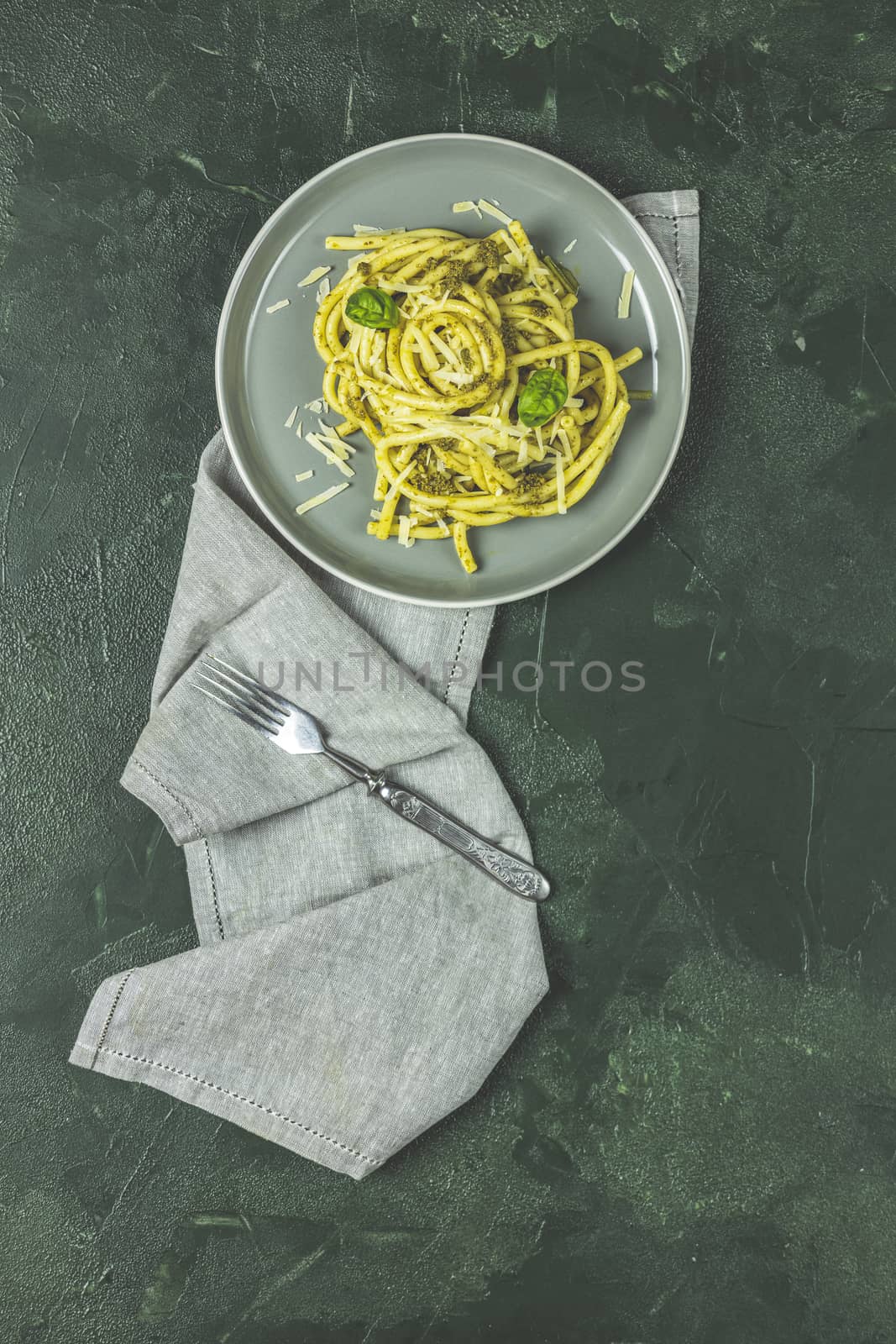 Spaghetti pasta bucatini with pesto sauce and parmesan. Italian traditional perciatelli pasta by genovese pesto sauce in gray dish. Flat lay on dark green surface.