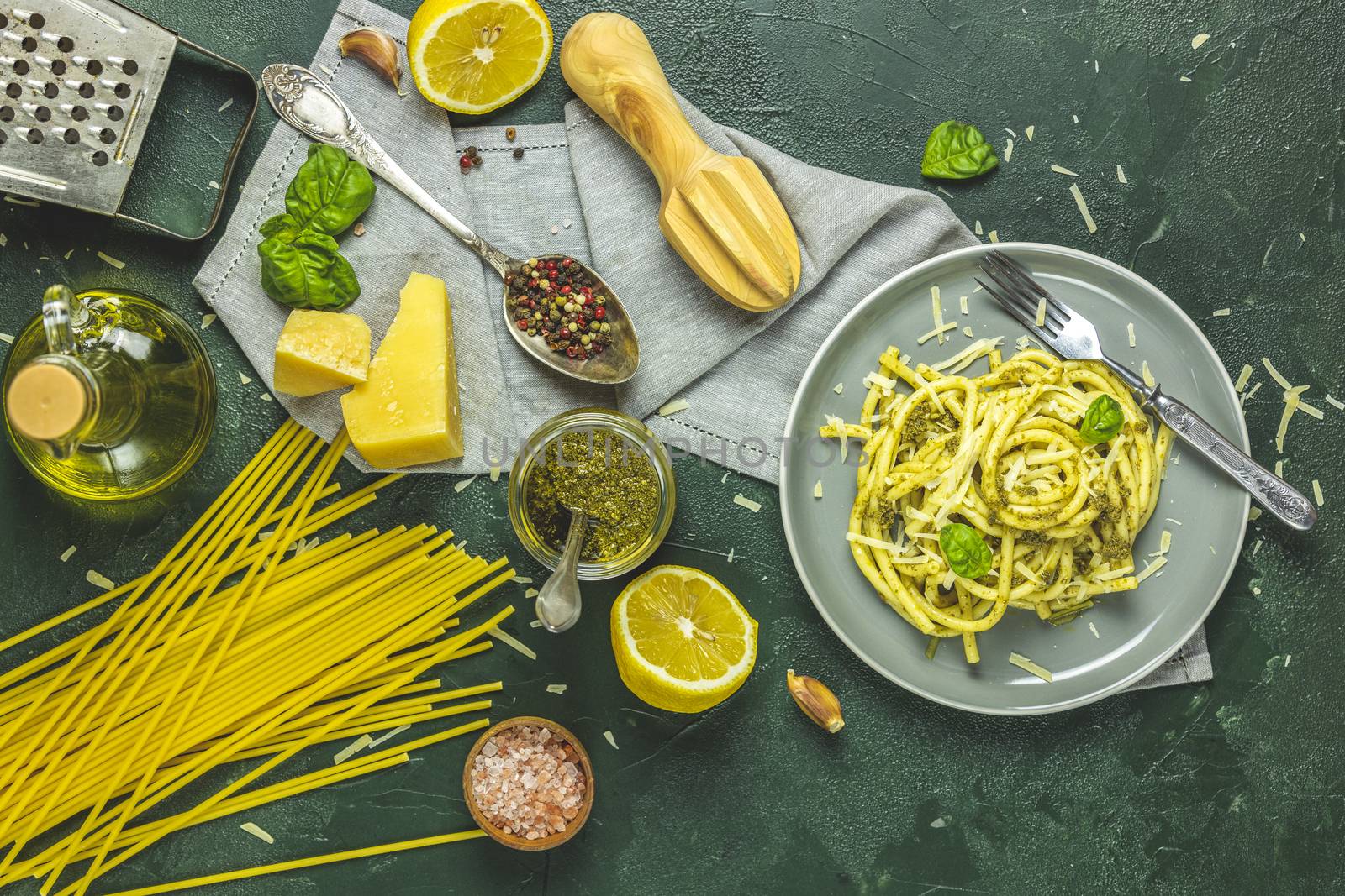 Gray plate of Italian traditional perciatelli pasta by genovese pesto sauce served with ingredients on dark green concrete table. Flat lay on dark green surface.	