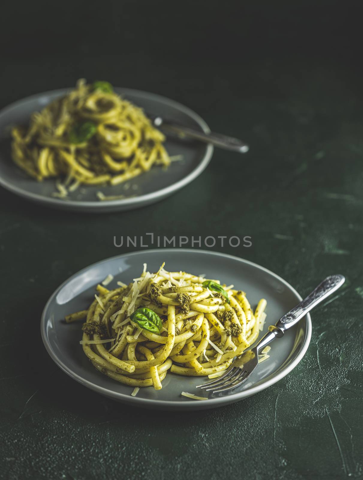 Spaghetti pasta bucatini with pesto sauce and parmesan. Italian traditional perciatelli pasta by genovese pesto sauce in two gray dishes	