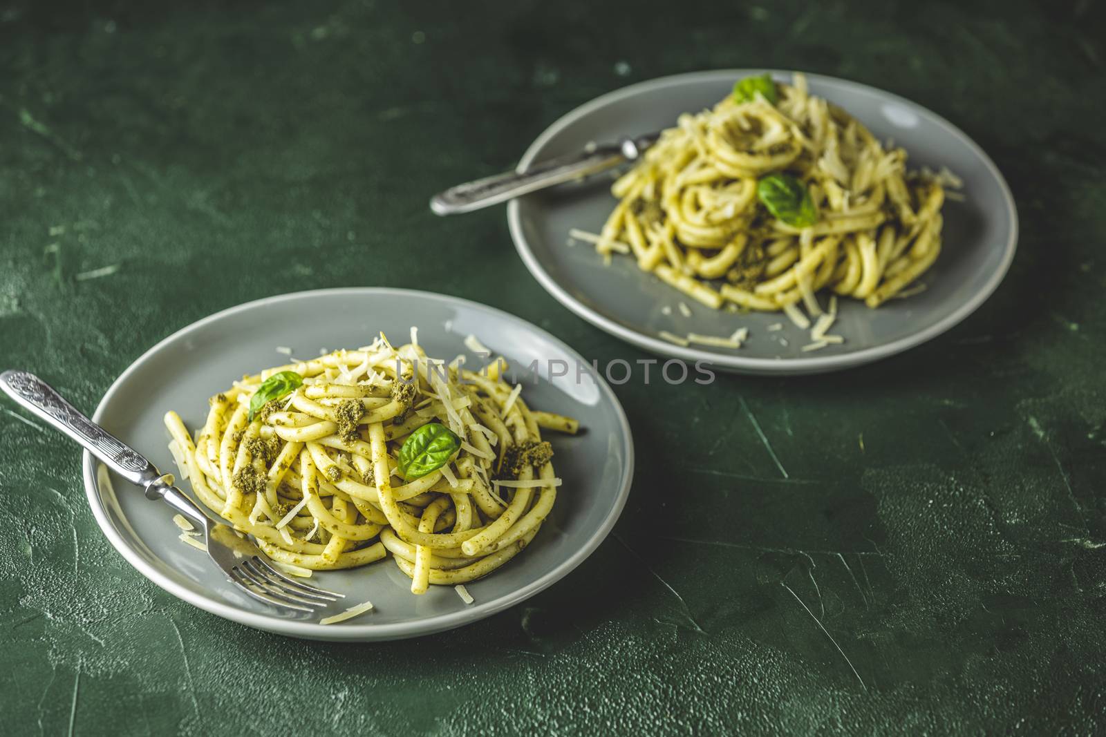 Two gray dishes of spaghetti pasta bucatini with pesto sauce and parmesan. Italian traditional perciatelli pasta by genovese pesto sauce