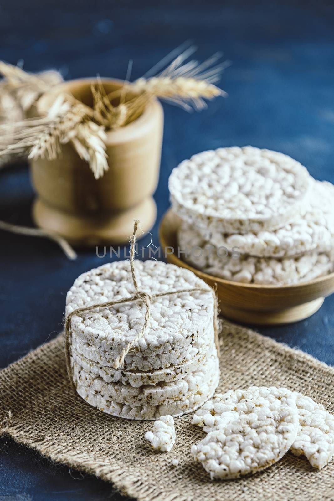 Stack of rice cakes. American puffed rice cakes. Healthy snacks with ears of wheat on classic blue concrete surface. Color of 2020 year. Classic Blue.