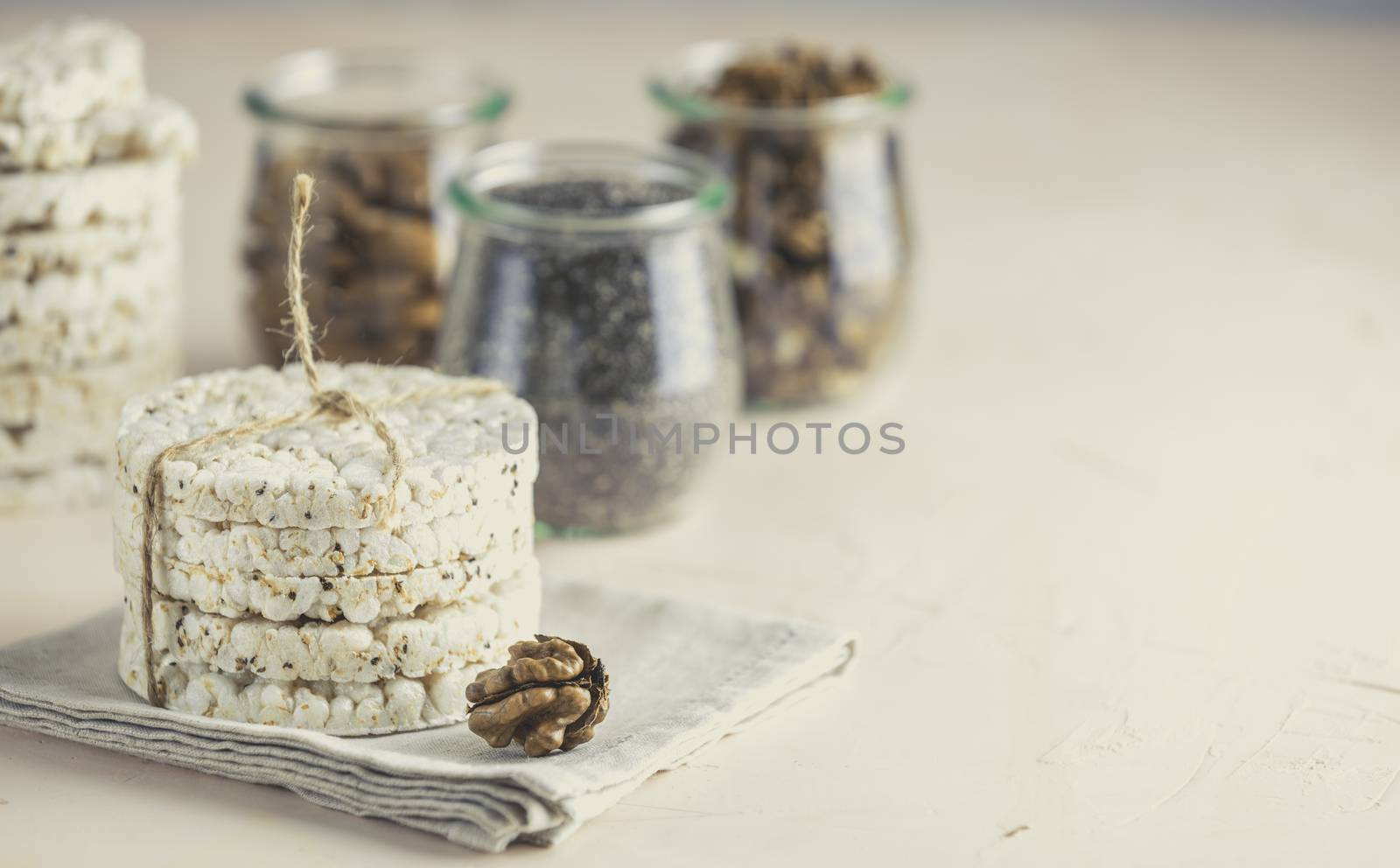 American puffed rice cakes. Healthy snacks with almonds, raisins, peanuts, pistachios in glass jars on light pink concrete surface.