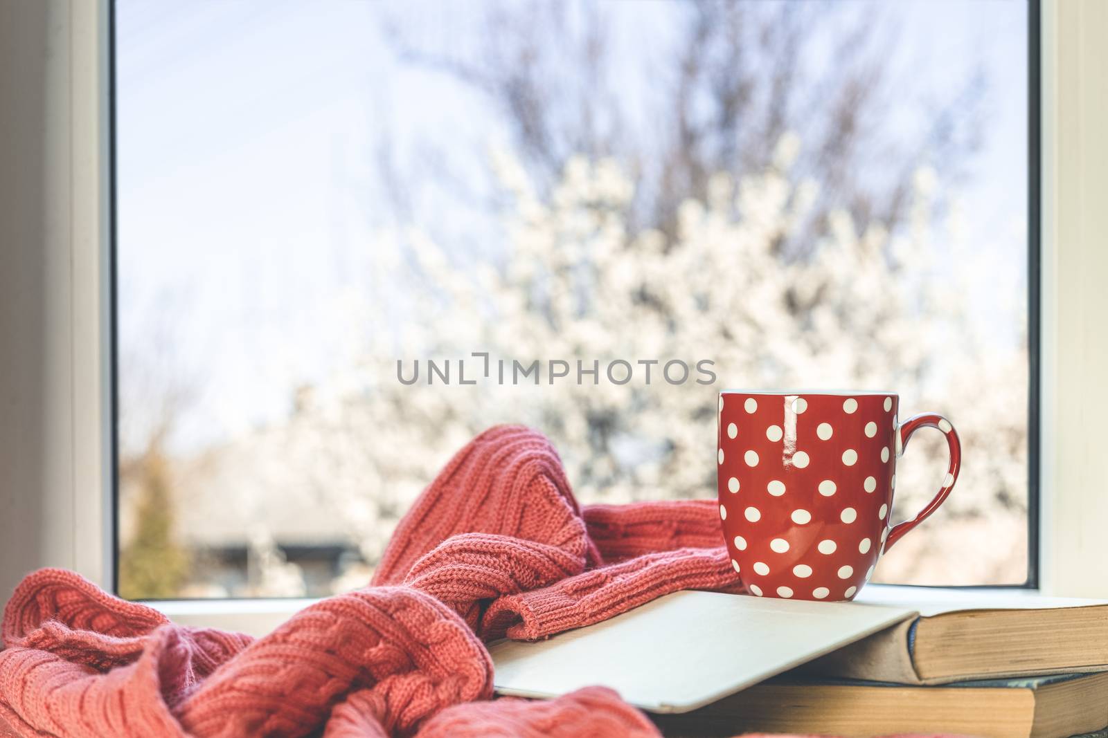 Red in white dotted cup of coffee of coffee on the window sill. In the background, a beautiful spring landscape. Cozy home concept. Stay at home and relax.