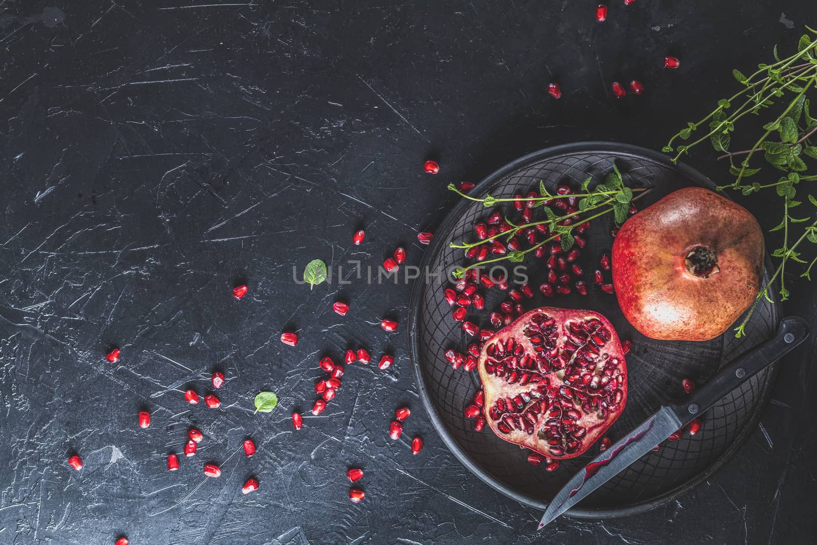 Fresh juicy pomegranate - whole and cut on a black vintage background, top view, horizontal, with copy space	