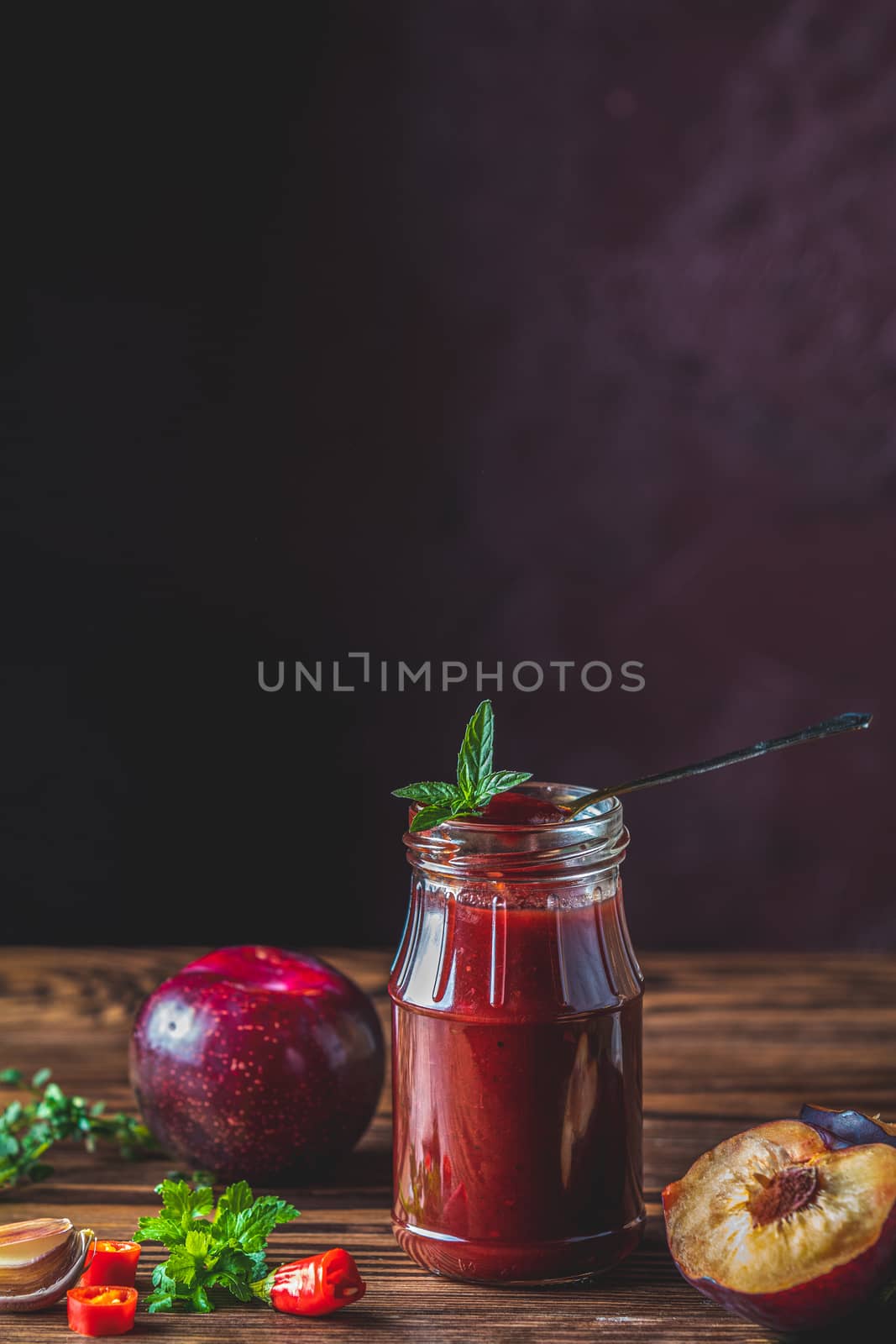 Homemade DIY natural canned hot plum sauce chutney with chilli or tkemali in glass jar standing on wooden table with ingredients — plum, salt, pepper,  herbs, selective focus