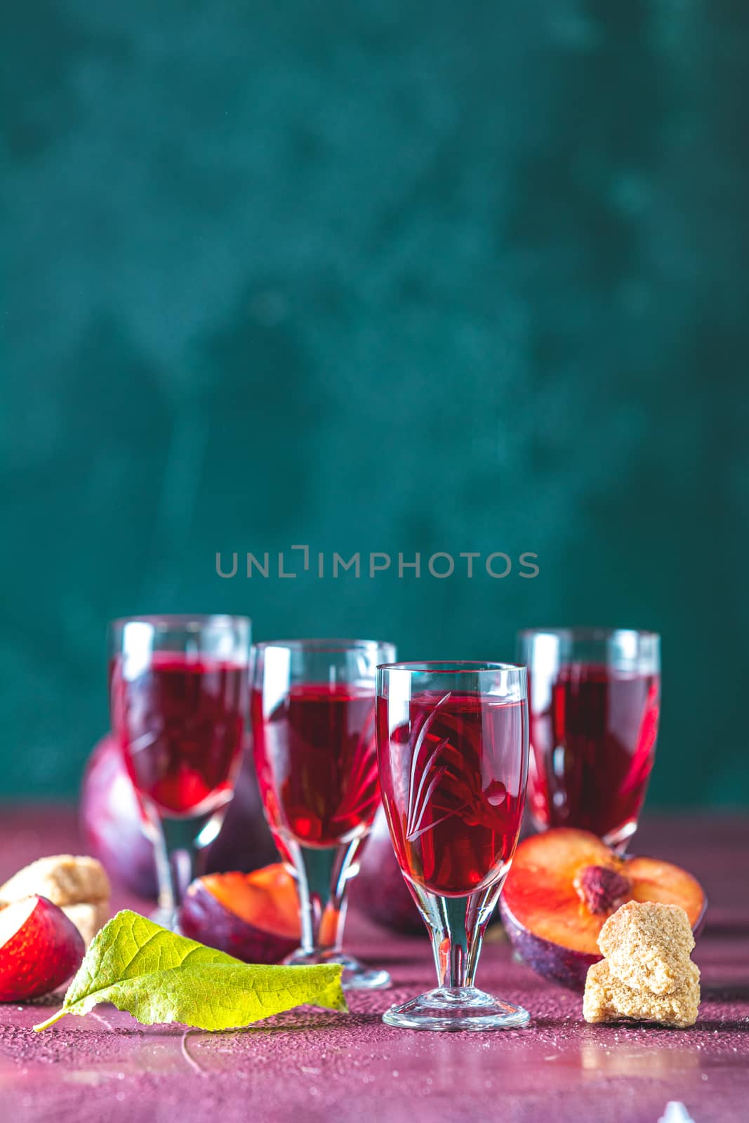 Plums strong alcoholic drink in shots. Hard liquor, slivovica, plum brandy or plum vodka with ripe plums on dark green and  claret bordeaux concrete surface.