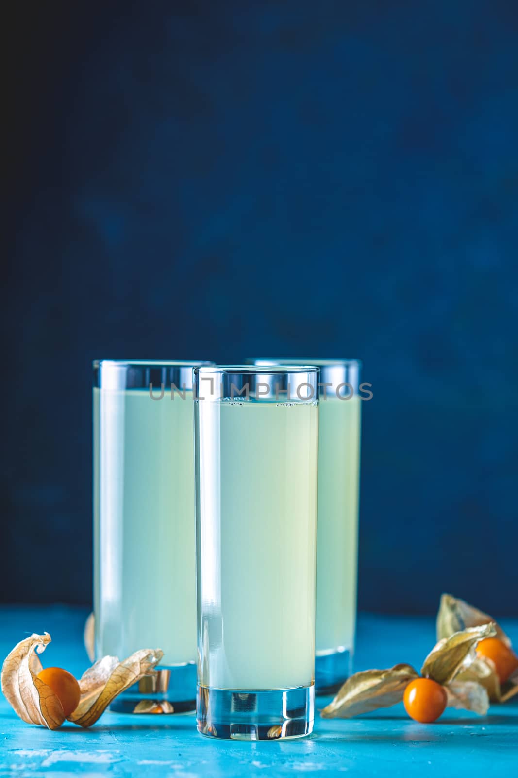 Alcoholic cocktail with Ouzo greek anise brandy or Arabic alcohol drink Raki in highball glass, decorated Physalis peruviana and brown sugar on blue concrete surface.