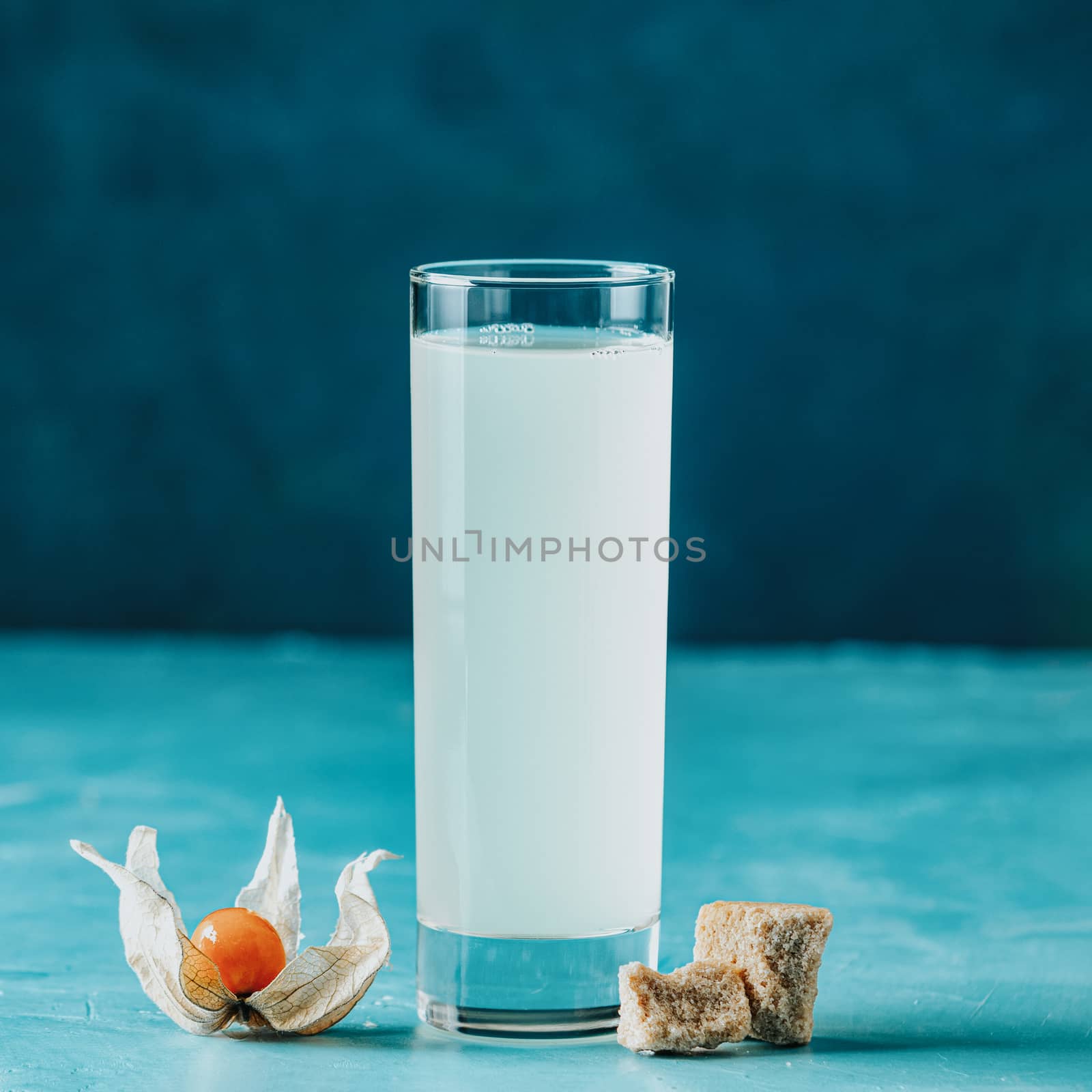 Alcoholic cocktail with Ouzo greek anise brandy or Arabic alcohol drink Raki in highball glass, decorated Physalis peruviana and brown sugar on blue concrete surface.