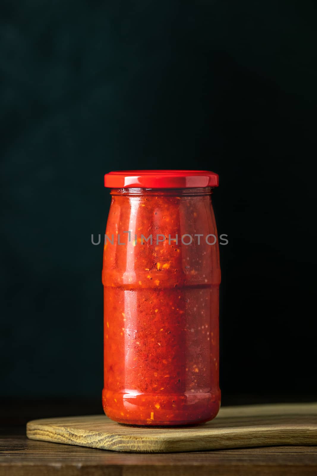 Homemade DIY natural canned hot tomato sauce chutney with chilli or adjika in glass jar standing on wooden table, selective focus