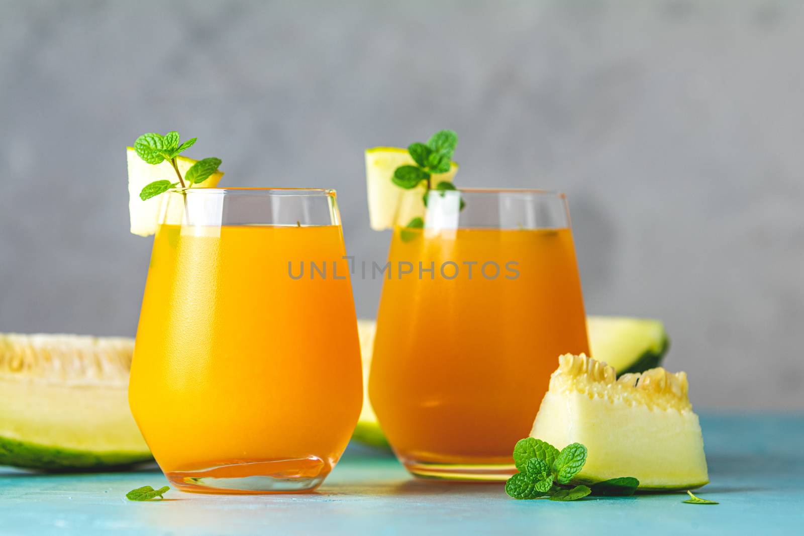 Yellow orange cocktail with melon and mint in glass on blue concrete background, close up. Summer drinks and alcoholic cocktails. Alcoholic or detox cocktail