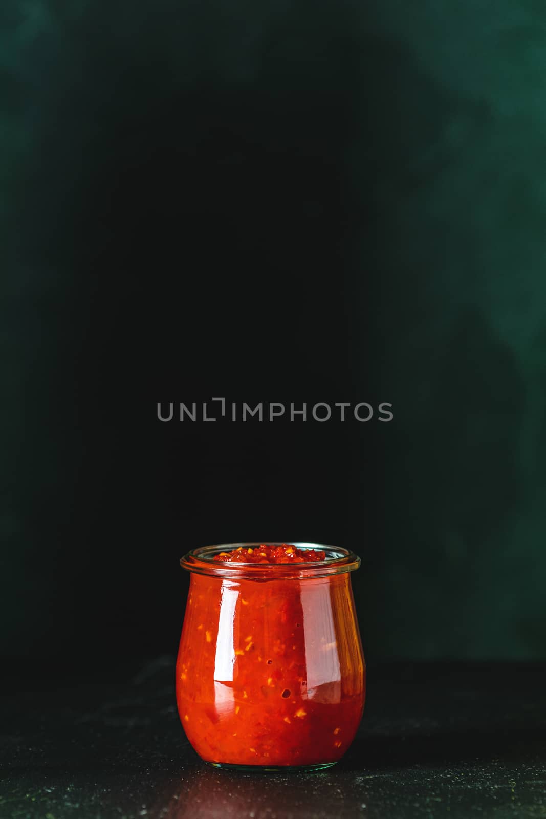 Homemade DIY natural canned hot tomato sauce chutney with chilli or adjika in glass jar standing on wooden table, selective focus, copy space for you text