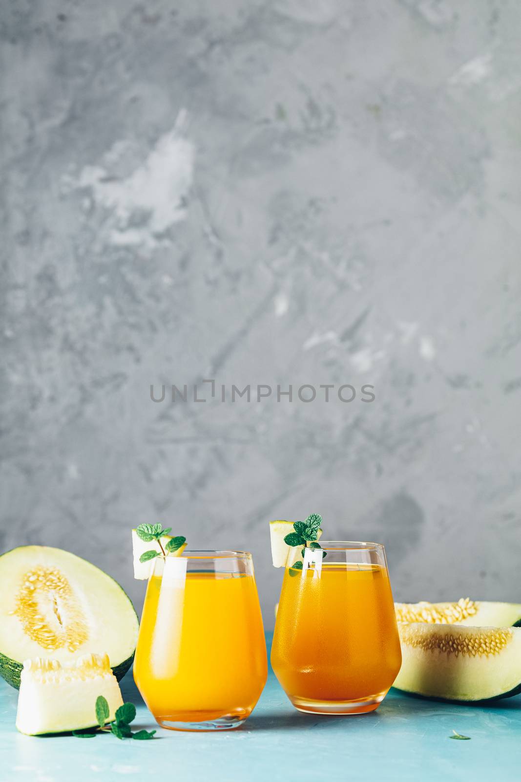 Yellow orange cocktail with melon and mint in glass on blue concrete background, close up. Summer drinks and alcoholic cocktails. Alcoholic or detox cocktail