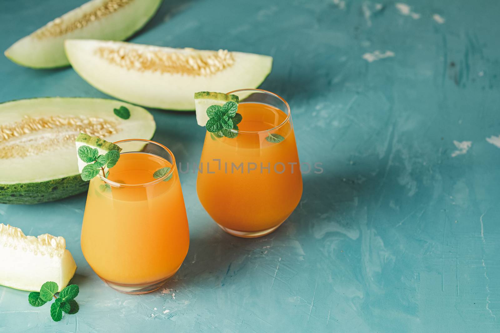 Yellow orange cocktail with melon and mint in glass on blue concrete background, close up. Summer drinks and alcoholic cocktails. Alcoholic or detox cocktail