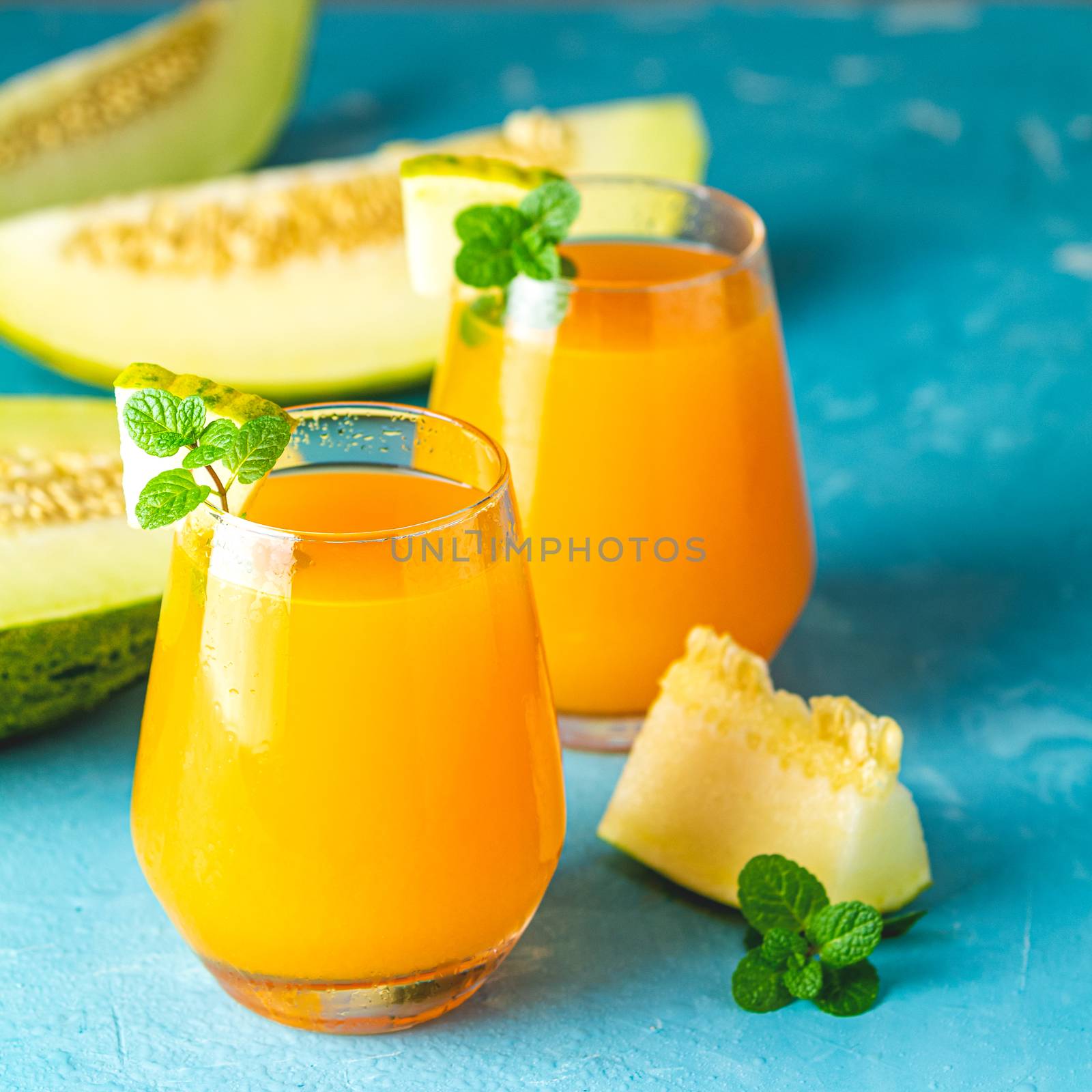 Yellow orange cocktail with melon and mint in glass on blue concrete background, close up. Summer drinks and alcoholic cocktails. Alcoholic or detox cocktail