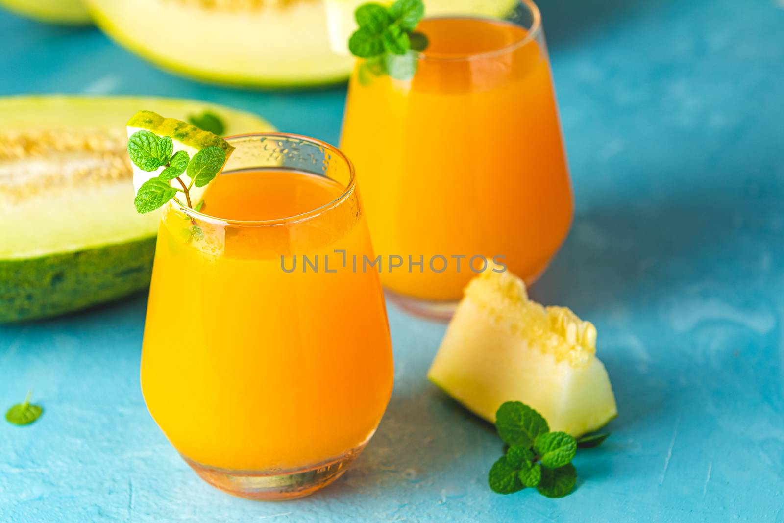 Yellow orange cocktail with melon and mint in glass on blue concrete background, close up. Summer drinks and alcoholic cocktails. Alcoholic or detox cocktail