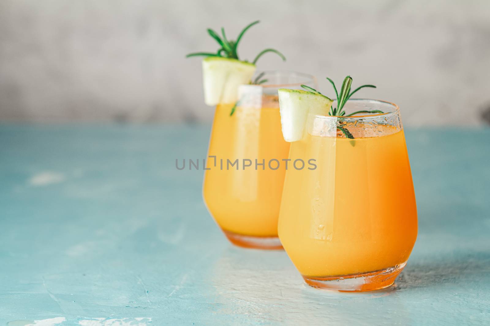 Yellow orange cocktail with melon and mint in glass on blue concrete background, close up. Summer drinks and alcoholic cocktails. Alcoholic or detox cocktail.