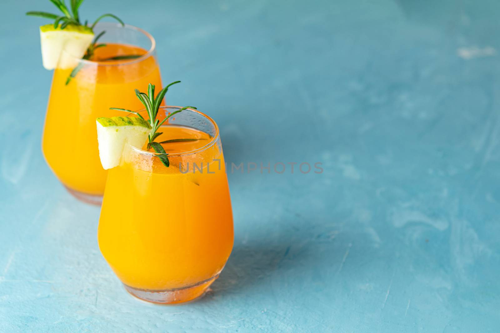 Yellow orange cocktail with melon and mint in glass on blue concrete background, close up. Summer drinks and alcoholic cocktails. Alcoholic or detox cocktail