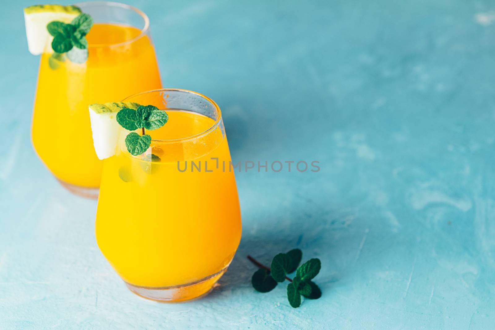 Yellow orange cocktail with melon and mint in glass on blue concrete background, close up. Summer drinks and alcoholic cocktails. Alcoholic or detox cocktail.