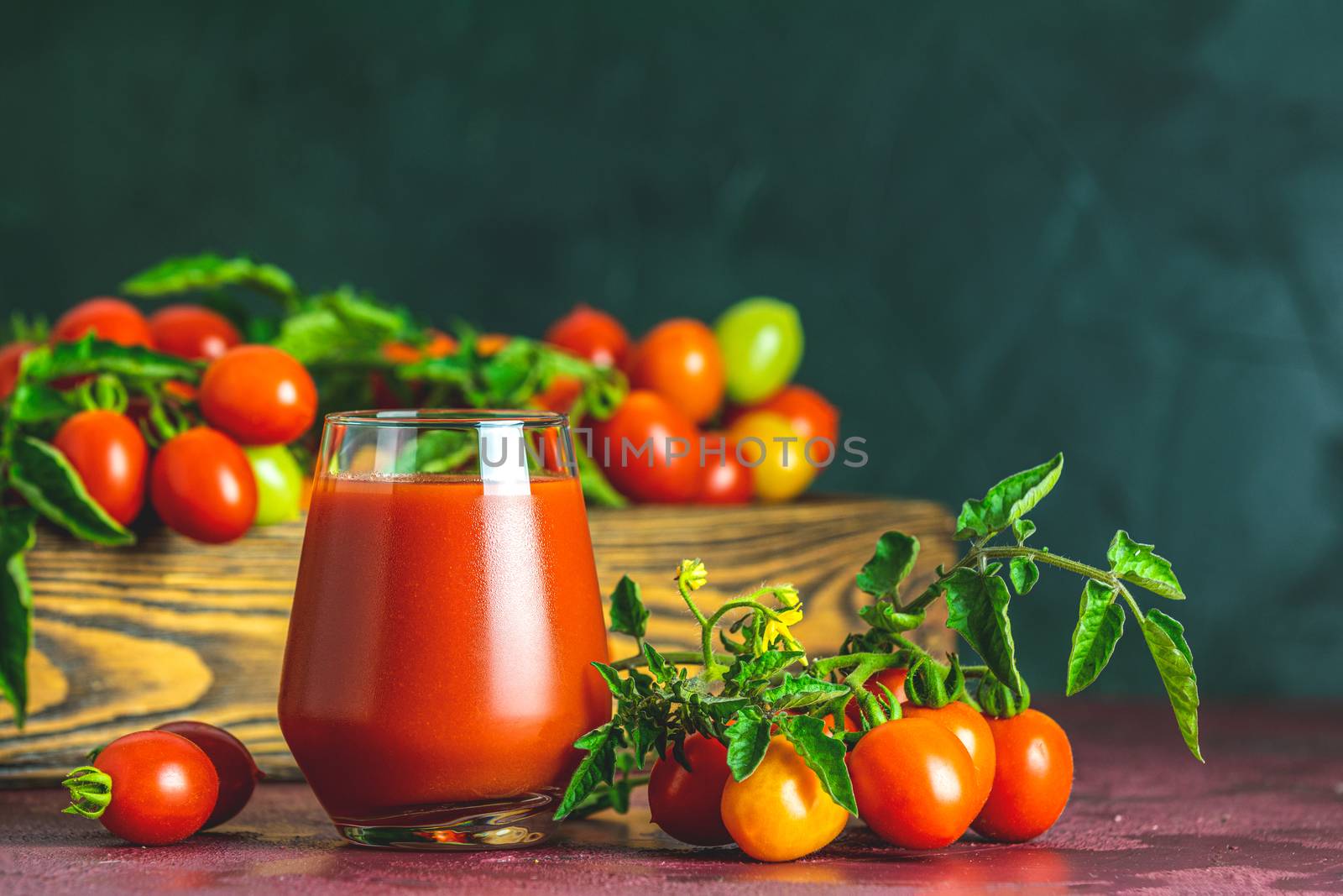 Glass of fresh delicious jummy red tomato juice and fresh tomatoes in wooden box. Dark background. Close up. Gmo free. Natural good food