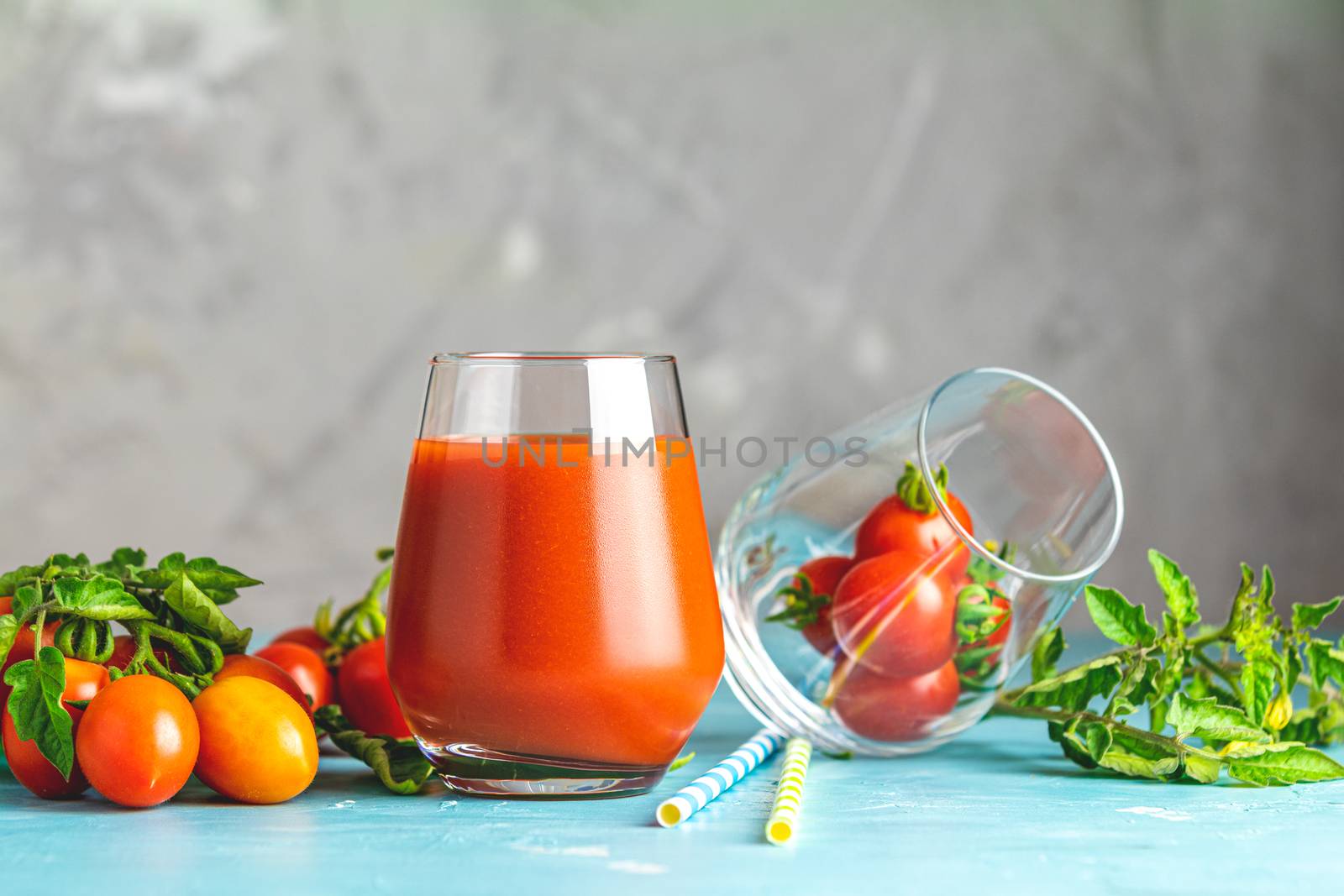 Glasses of fresh delicious jummy red tomato juice and fresh raw tomatoes with pink salt in spoon on light concrete surface. Close up. Gmo free. Natural good food.