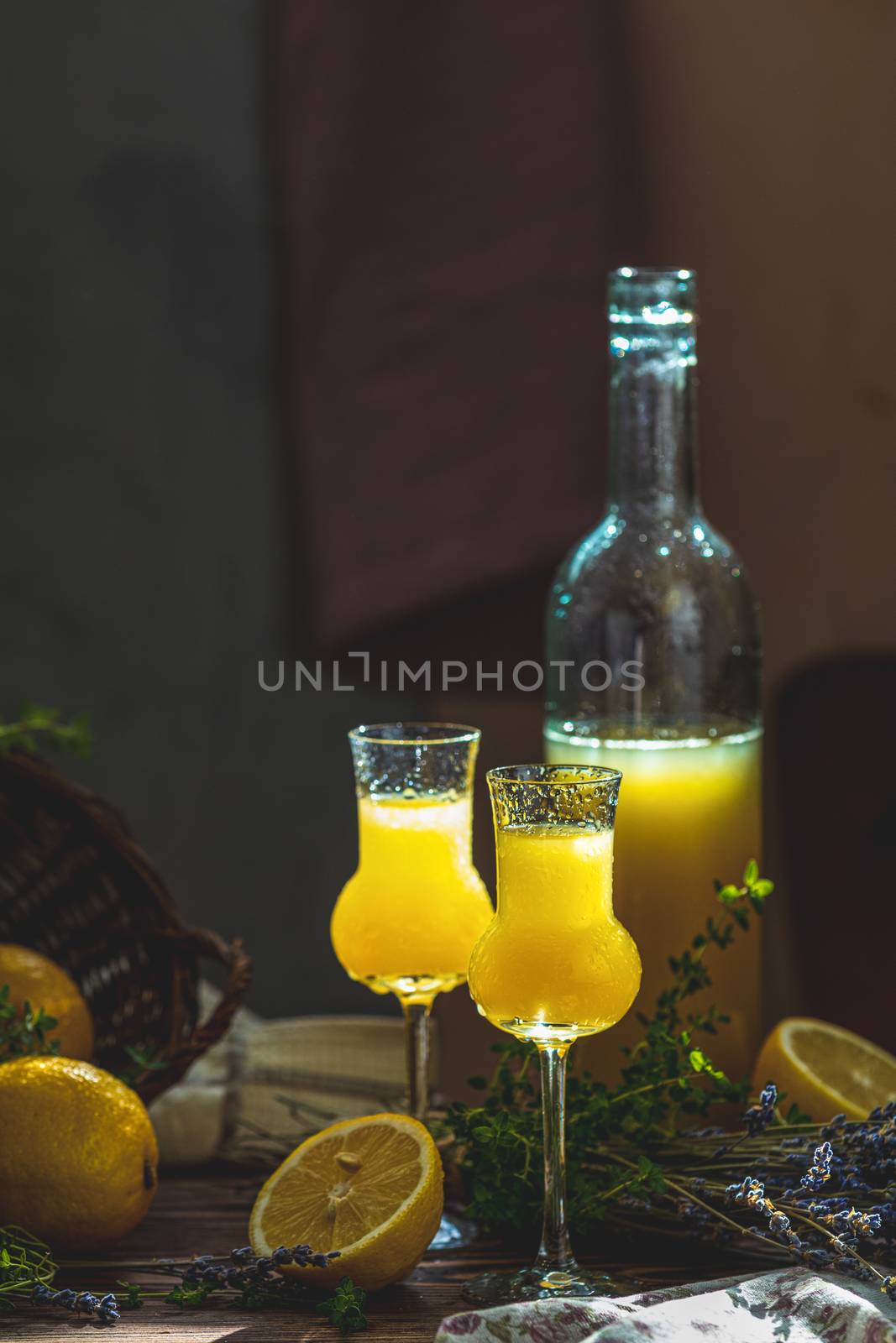 Limoncello in grappas wineglass with water drops and lavender on dark wooden table. Artistic still life on dark background with sunny light.