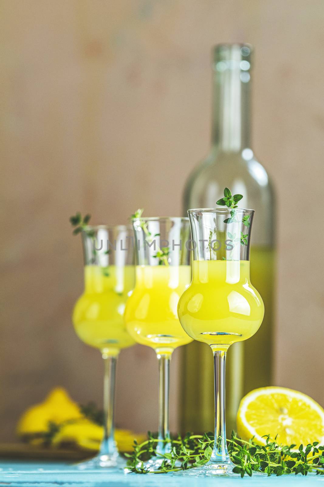 Limoncello with thyme in grappas wineglass with water drops on light concrete table. Artistic still life on light background with sunny light.