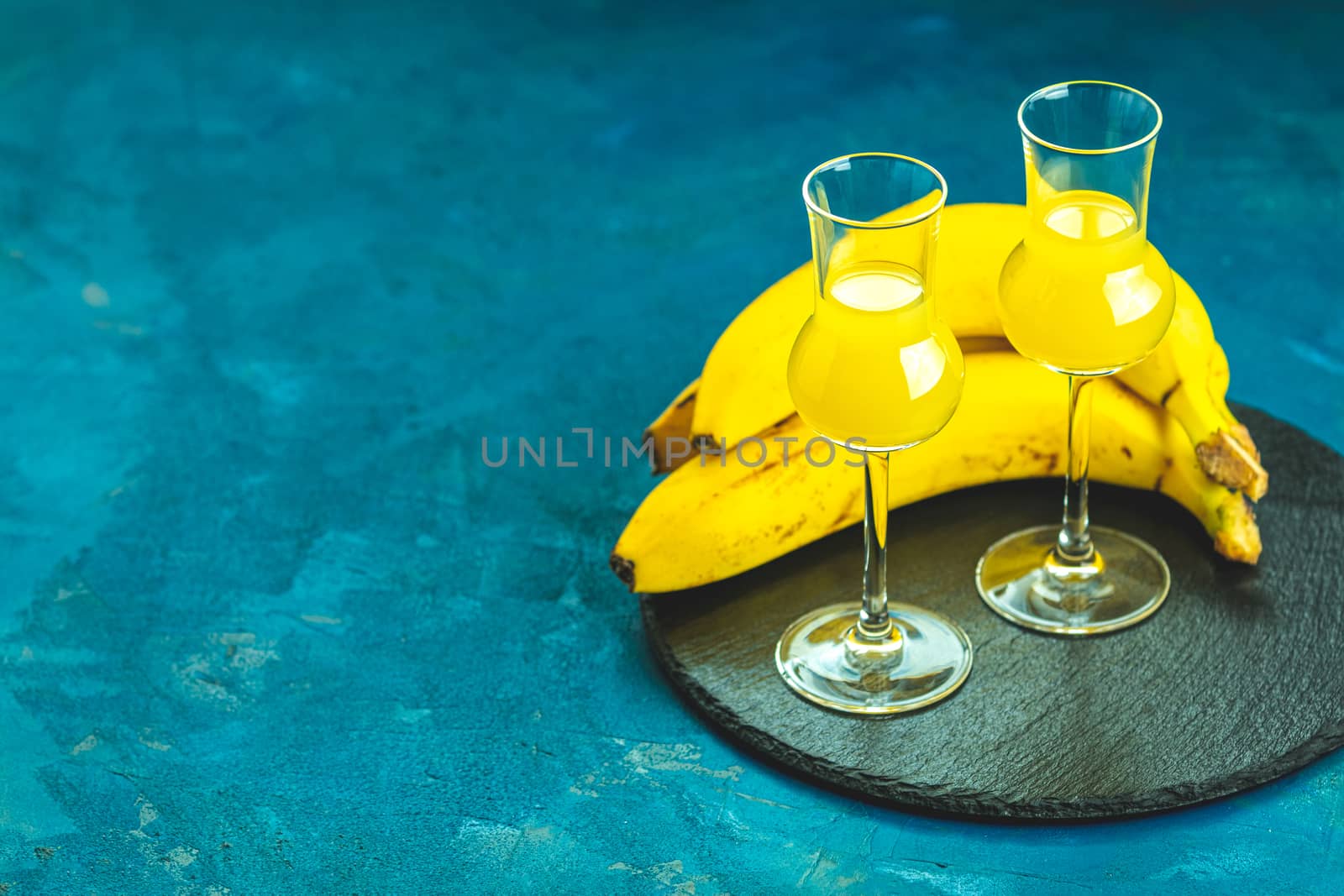 Banana flavoured liqueurs, which French call creme de banana, in  grappas wineglass on dark blue concrete surface. European aperitif drink. Selective focus, shallow depth of the fields, copy space.