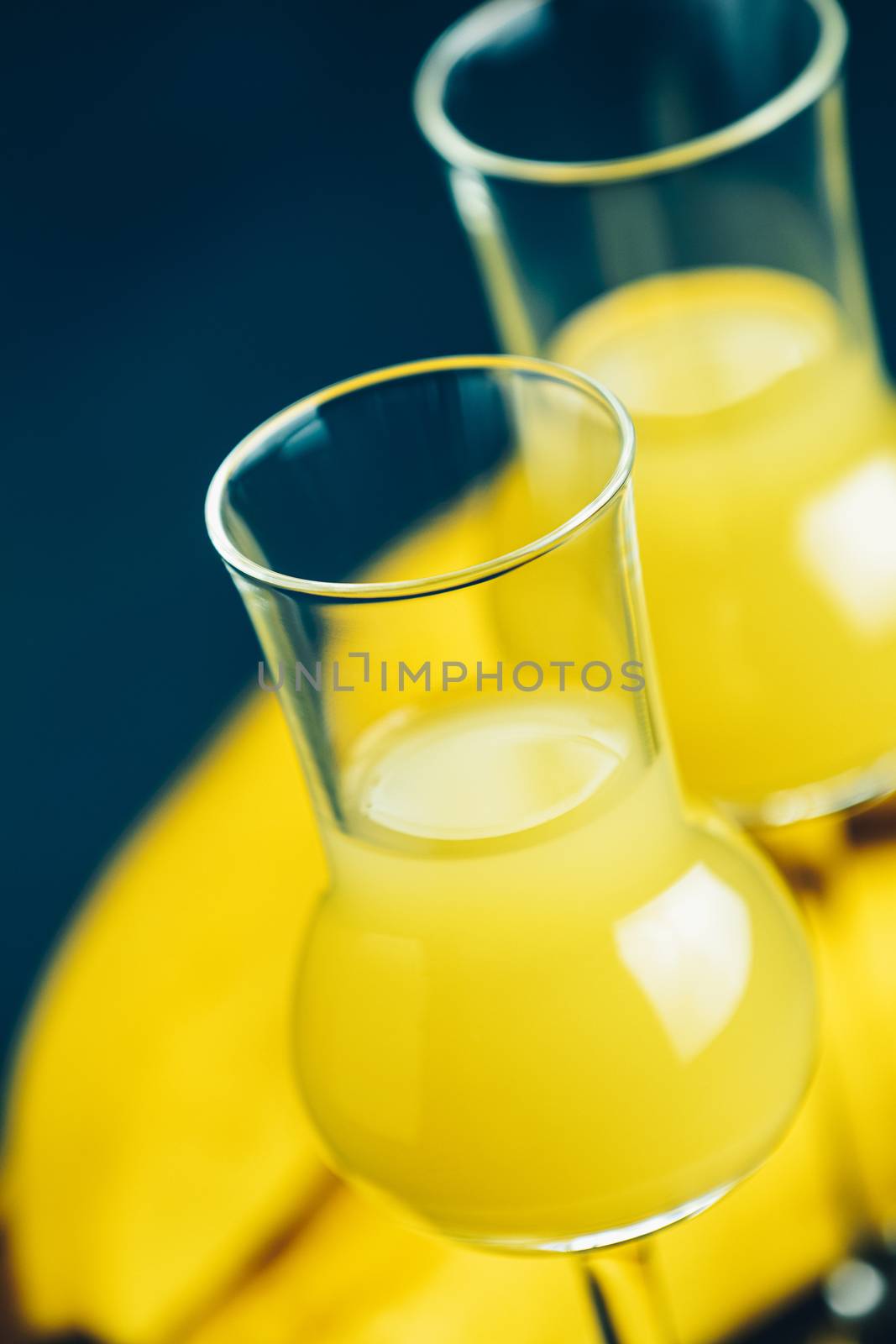 Banana flavoured liqueurs, which French call creme de banana, in  grappas wineglass on dark concrete surface. European aperitif drink. Selective focus, shallow depth of the fields, copy space.