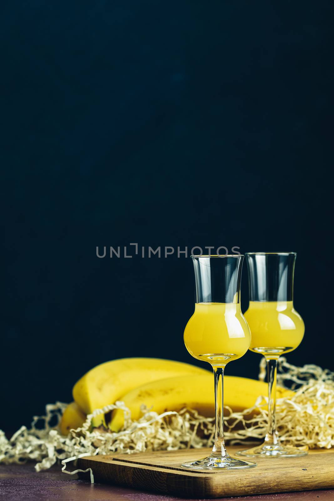 Banana flavoured liqueurs, which French call creme de banana, in  grappas wineglass on dark concrete surface. European aperitif drink. Selective focus, shallow depth of the fields, copy space.