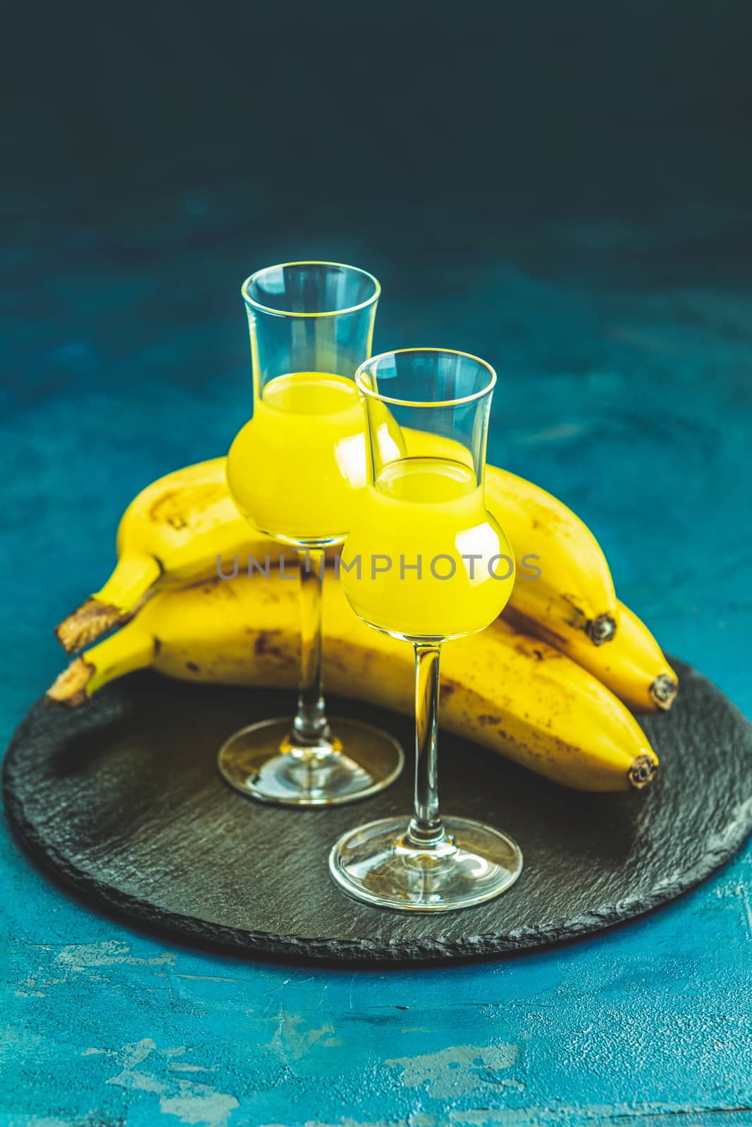 Banana flavoured liqueurs, which French call creme de banana, in  grappas wineglass on dark blue concrete surface. European aperitif drink. Selective focus, shallow depth of the fields, copy space.