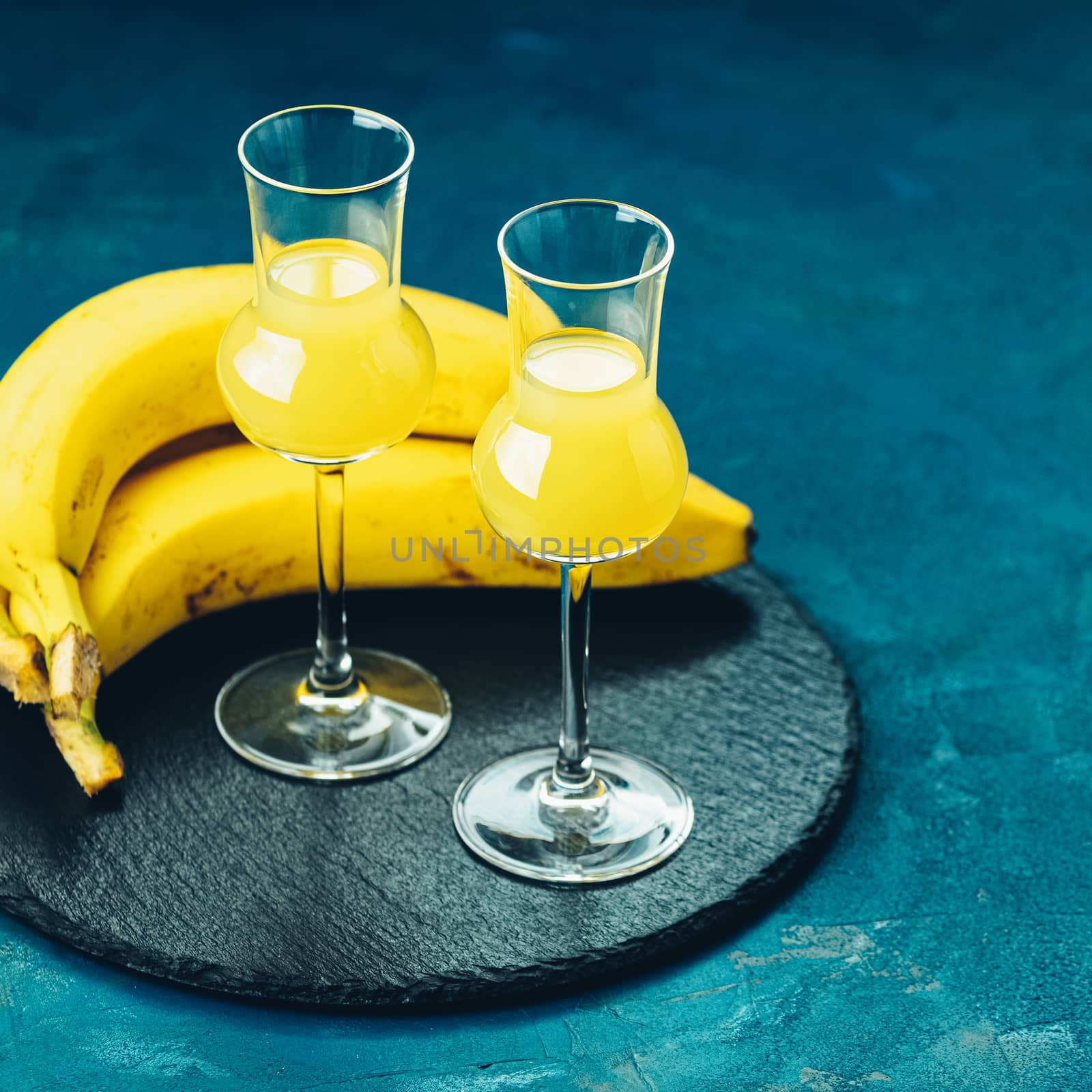 Banana flavoured liqueurs, which French call creme de banana, in  grappas wineglass on dark blue concrete surface. European aperitif drink. Selective focus, shallow depth of the fields, copy space.