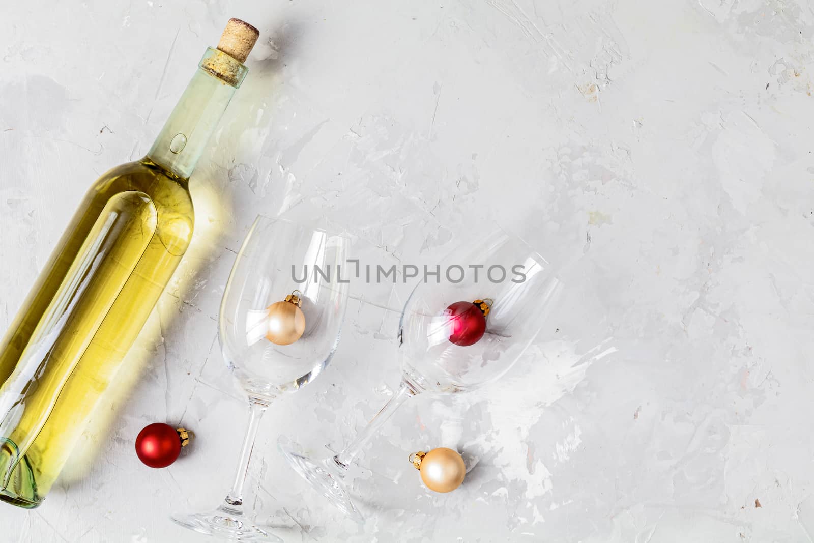 Creative food art background. Bottle of wine and two wineglasses with red and gold сhristmas balls on light gray concrete surface, top view, flat lay, copy space for you text.