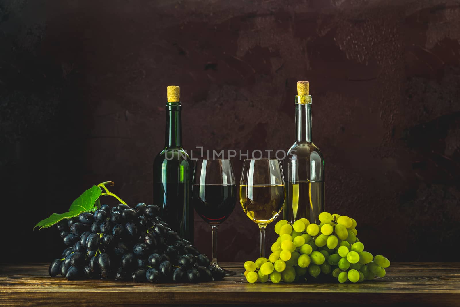 Glasses and bottles of wine and grapes on dark claret bordeaux concrete surface background