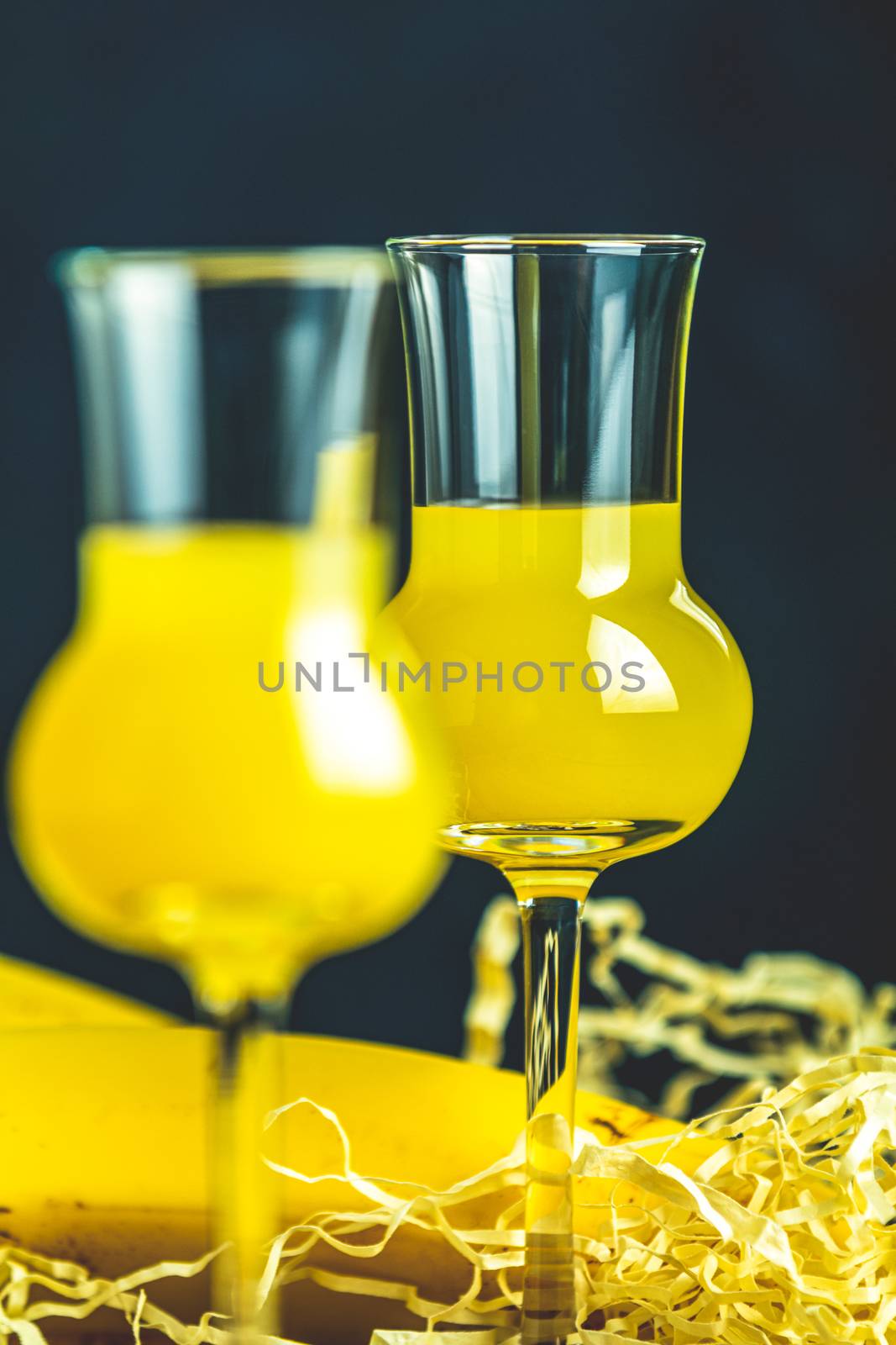 Banana flavoured liqueurs, which French call creme de banana, in  grappas wineglass on dark concrete surface. European aperitif drink. Selective focus, shallow depth of the fields, copy space.