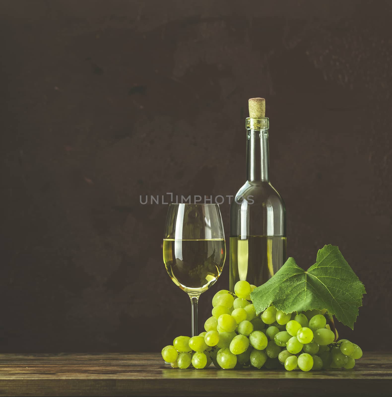 Glasses and bottles of wine and grapes on dark claret bordeaux concrete surface background.