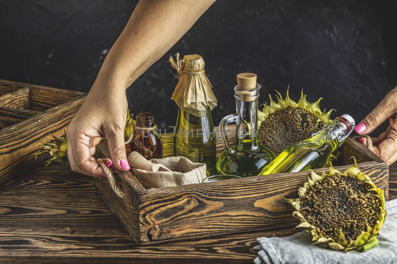 Female woman hands holding a tray with organic sunflower oil in a small glass jars with sunflower seeds. Closeup photo of sunflower oil with seeds on wooden background. Bio and organic product concept.