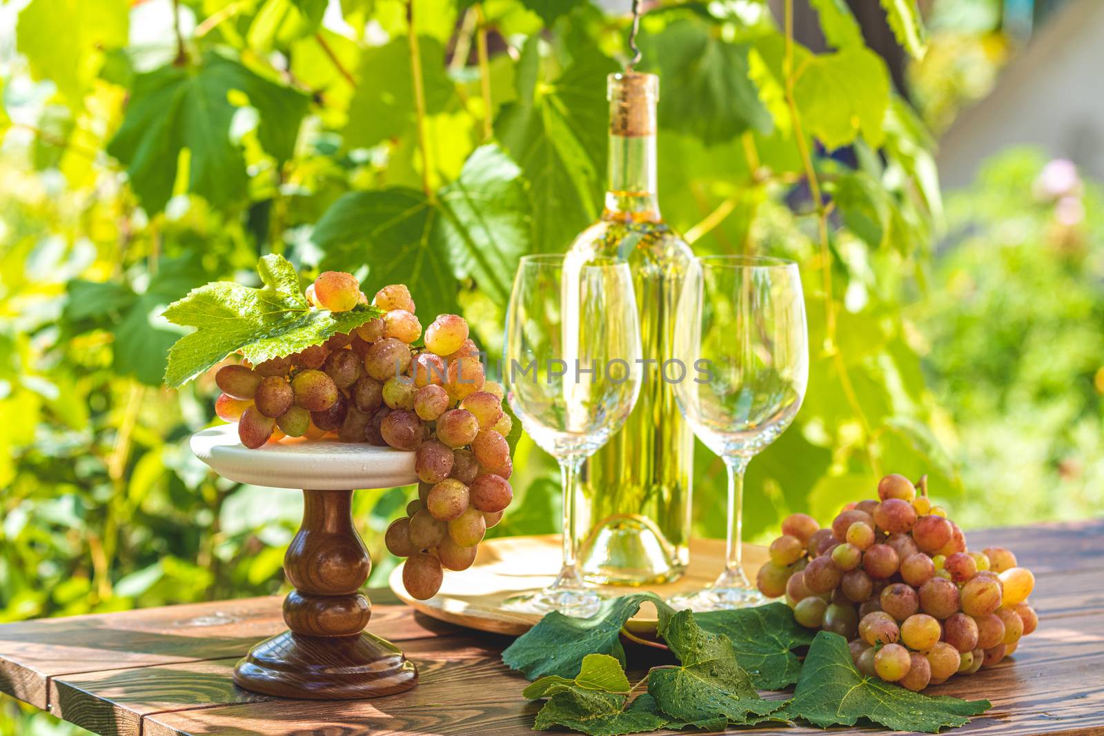 Grape and white wine. Green grape and white wine in vineyard. Bunch of grapes with water drops on the table. Sunny garden with vineyard background.