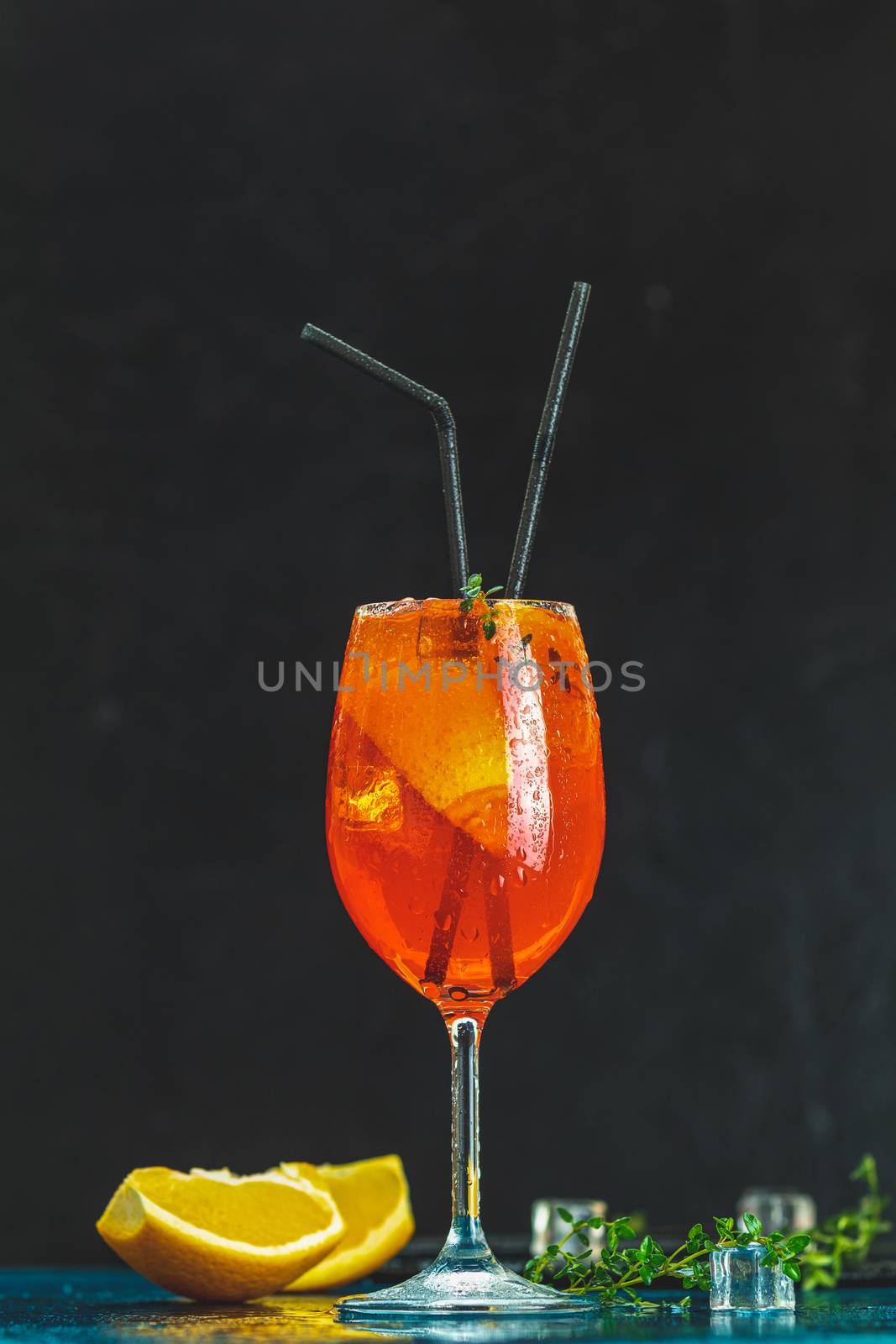 Cocktail aperol spritz in big wine glass with water drops on dark background. Summer alcohol cocktail with orange slices. Italian cocktail aperol spritz on slate board