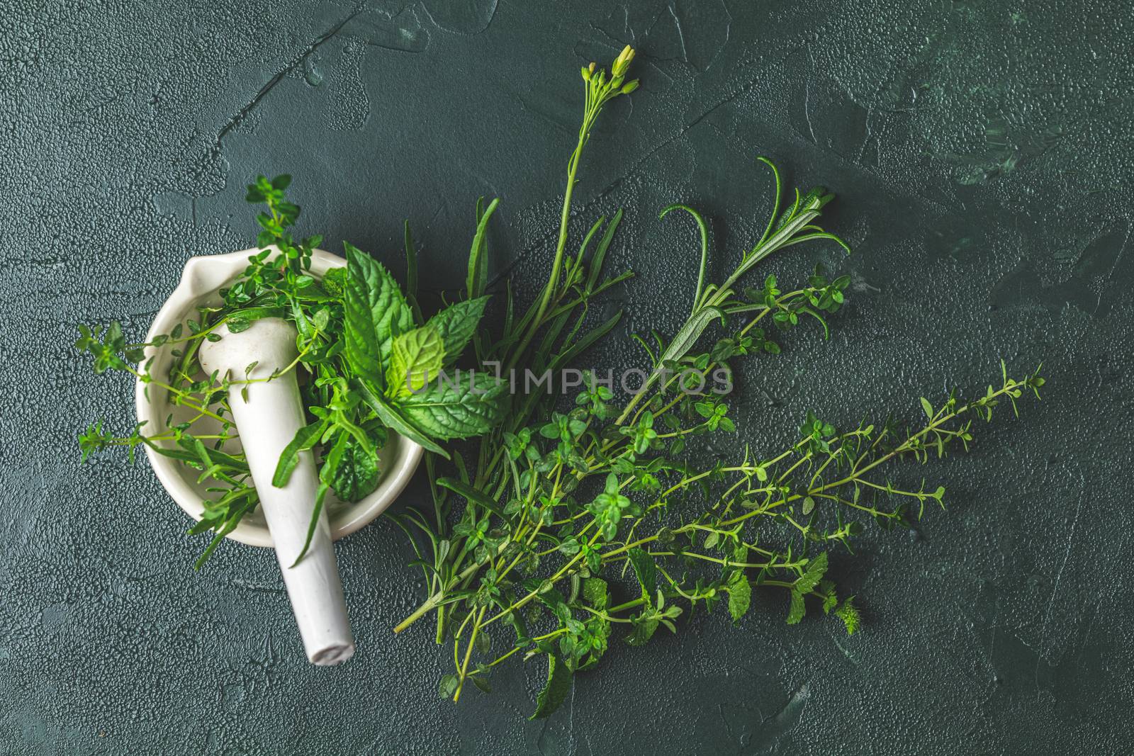 Mortar with herbs and spices. Fresh herbs selection included rosemary, thyme, mint, lemon balm, parsley and arugula. Overhead view, copy space. Dark green concrete surface.
