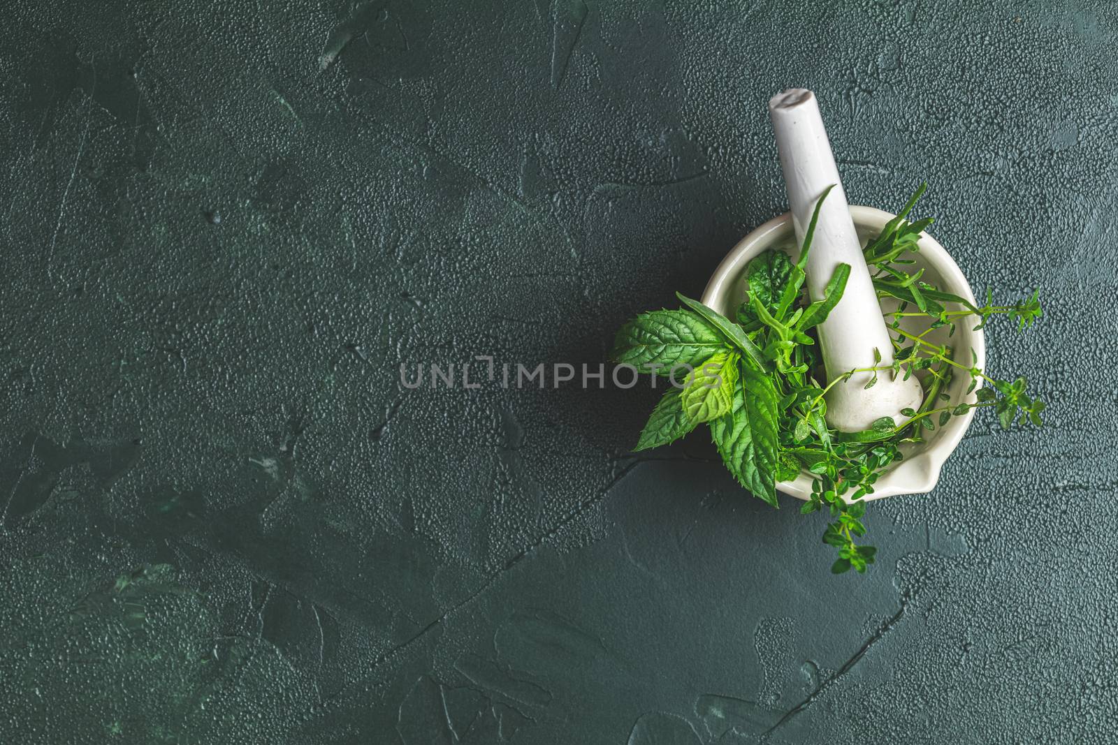 Mortar with  herbs and spices. Fresh herbs selection included rosemary, thyme, mint, lemon balm, parsley and arugula. Overhead view, copy space. Dark green concrete surface.